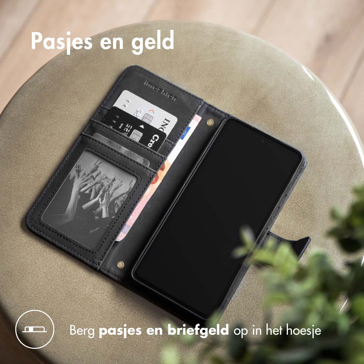 Een open zwarte portemonnee op een tafel. Het toont kaarten, contant geld en heeft een telefoon. Tekst zegt 'Pasjes en geld'.