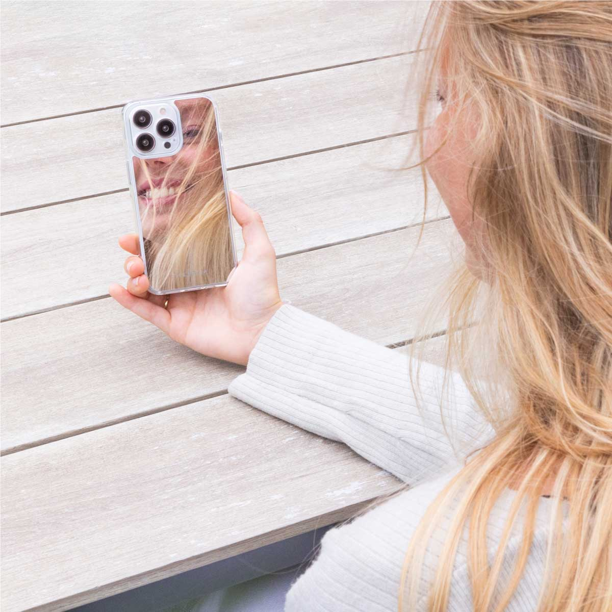 Blonde vrouw maakt selfie met haar telefoon, toont reflectie van haar gezicht. Ze is op houten oppervlak.