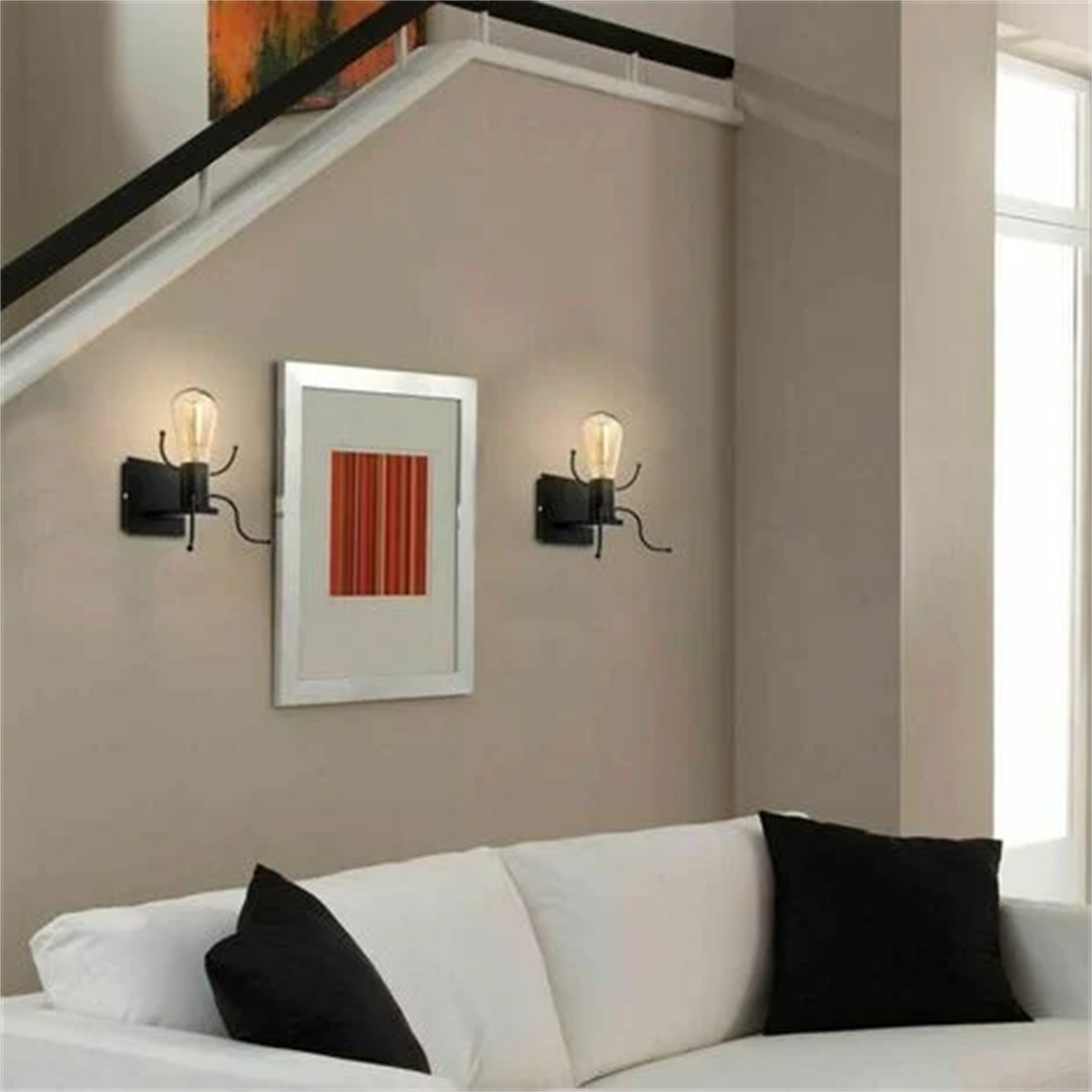 Wandleuchten mit Glühbirnen. Ein gerahmtes Bild an einer Wand mit weißem Sofa und schwarzen Kissen.