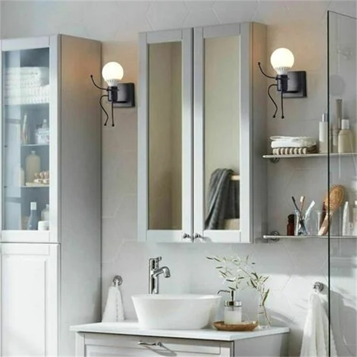 Zwei Wandlampen in einem Badezimmer. Jede hat einen Glühbirnenkopf und eine Personenform.