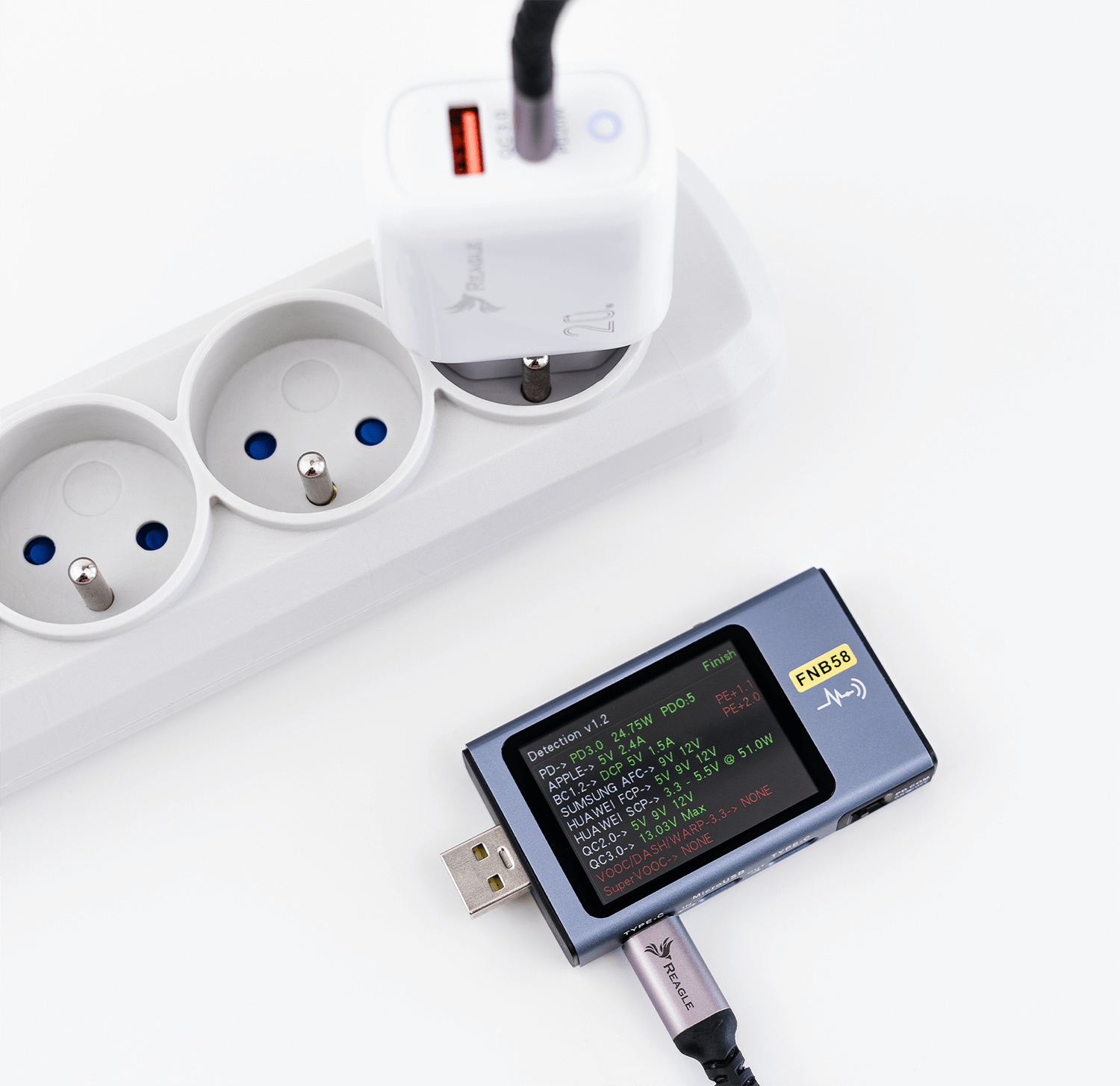 Biała listwa zasilająca z podłączoną ładowarką i czarne urządzenie na białej powierzchni.