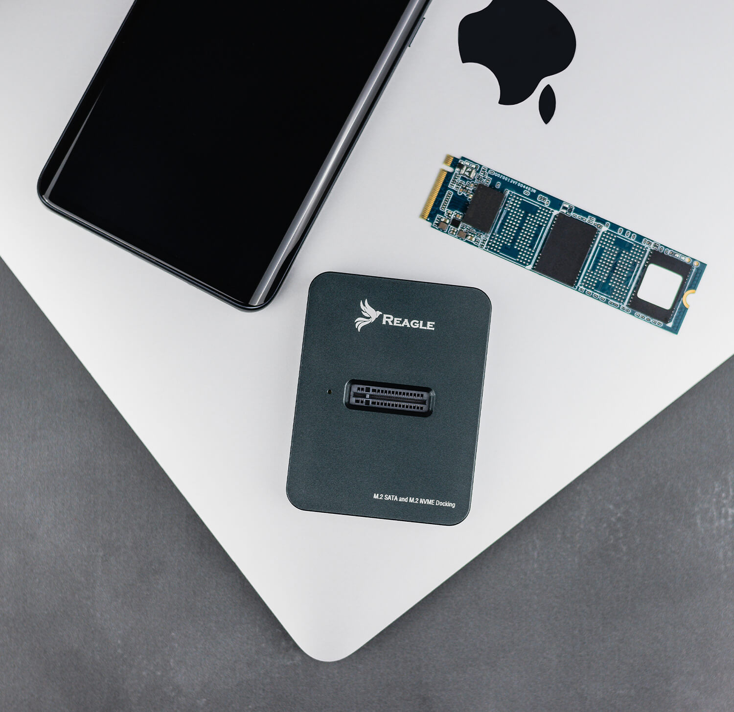 SSD-Laufwerk, Dockingstation und Smartphone auf einem Laptop. Alles auf weißer Oberfläche.