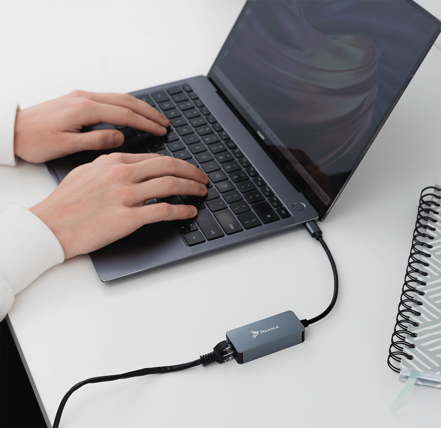 Osoba korzystająca z laptopa podłączonego do małego szarego urządzenia przez USB.