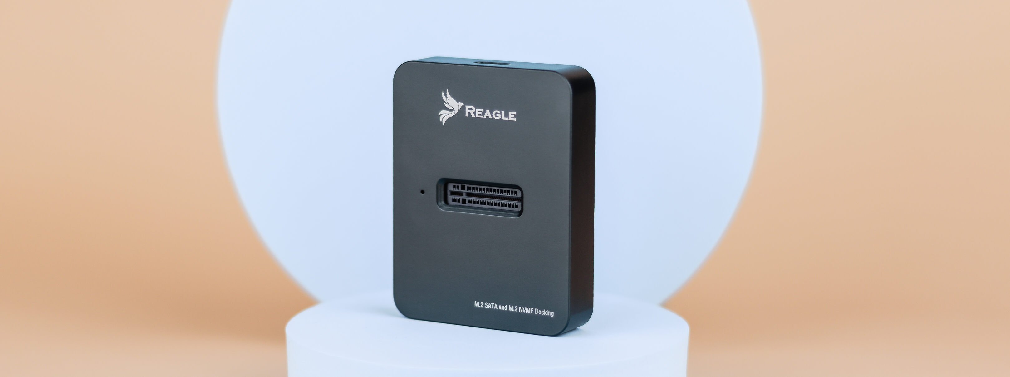 Schwarzes Reagle-Gerät, M.2 SATA und M.2 NVMe. Rechteckig, mit Logo. Hellorangefarbener Hintergrund.
