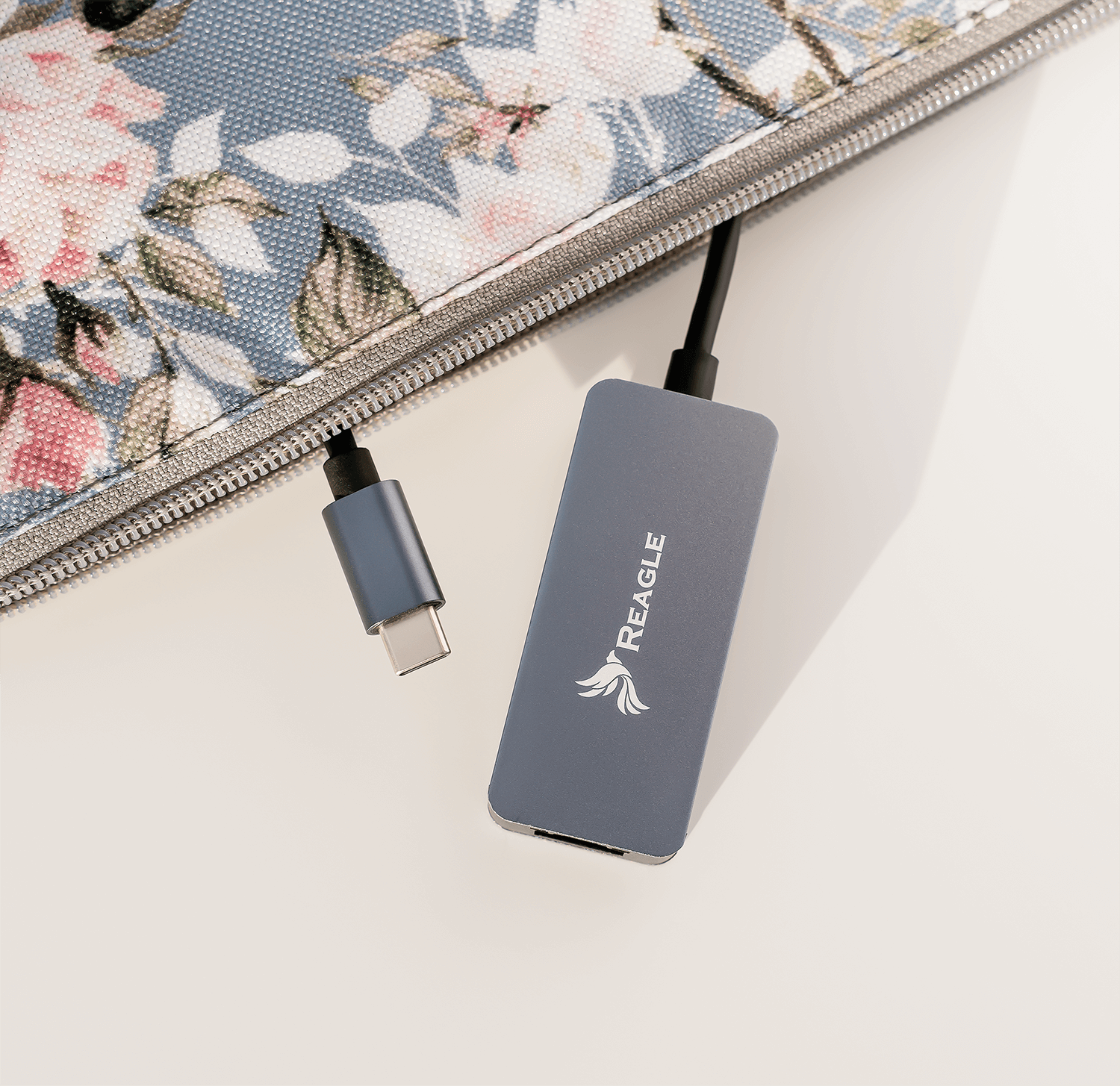 Szara przejściówka USB-C Reagle i kabel USB-C, w pobliżu etui z kwiatowym wzorem.