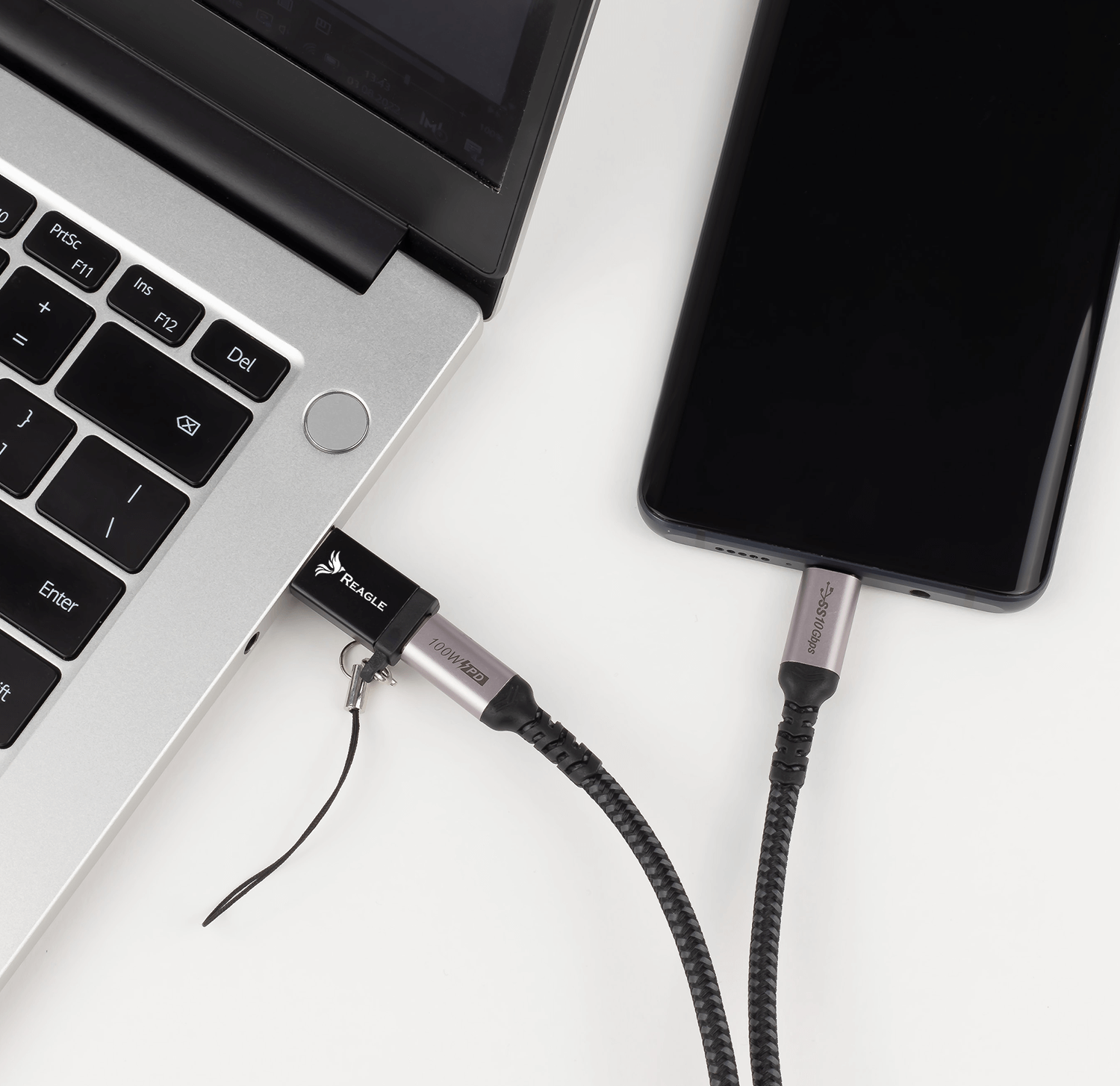 Laptop i telefon połączone kablem USB-C, na białej powierzchni.