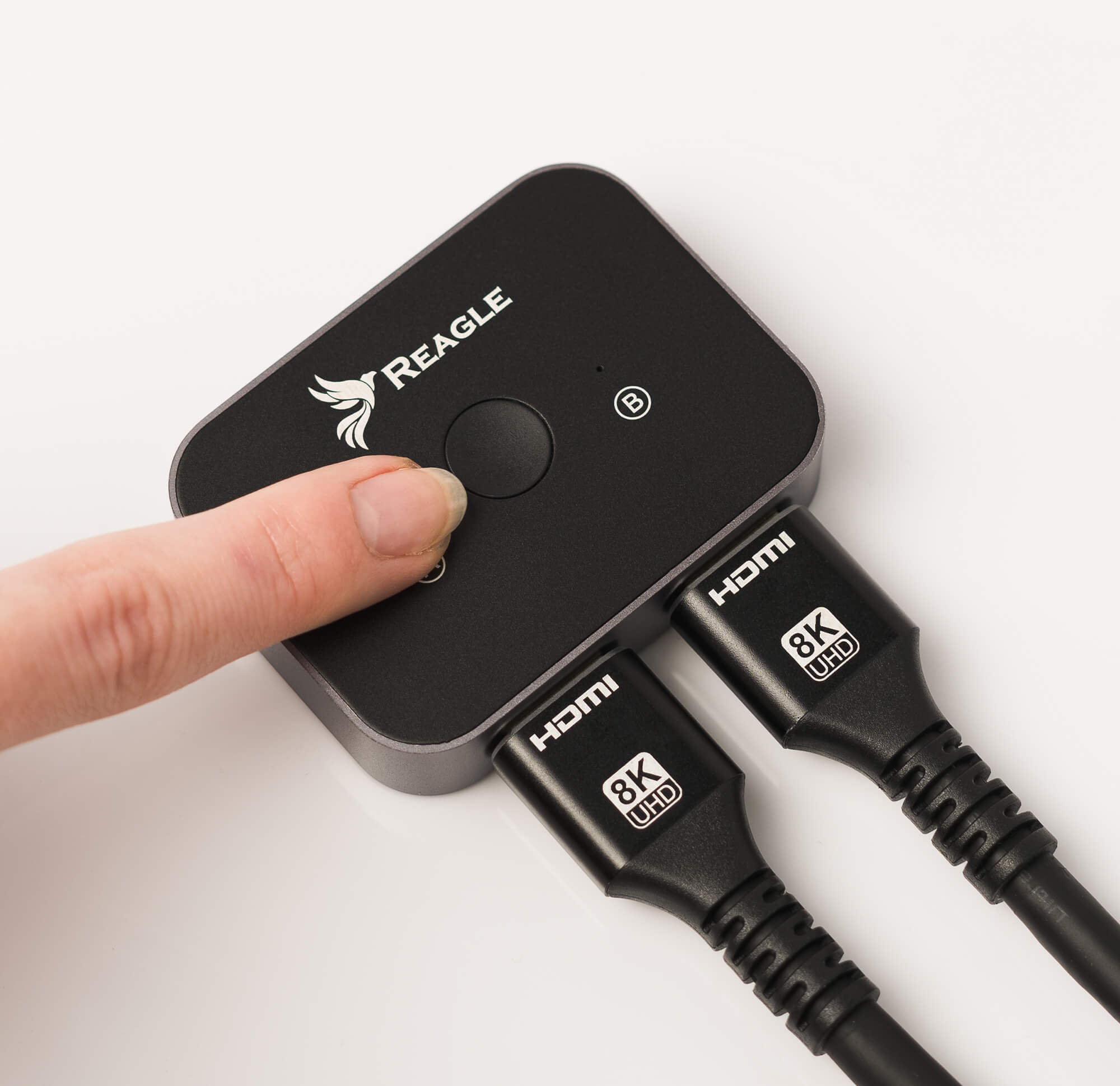 Czarny przełącznik HDMI. Dwa kable HDMI podłączone. Palec naciska przycisk. Białe tło.