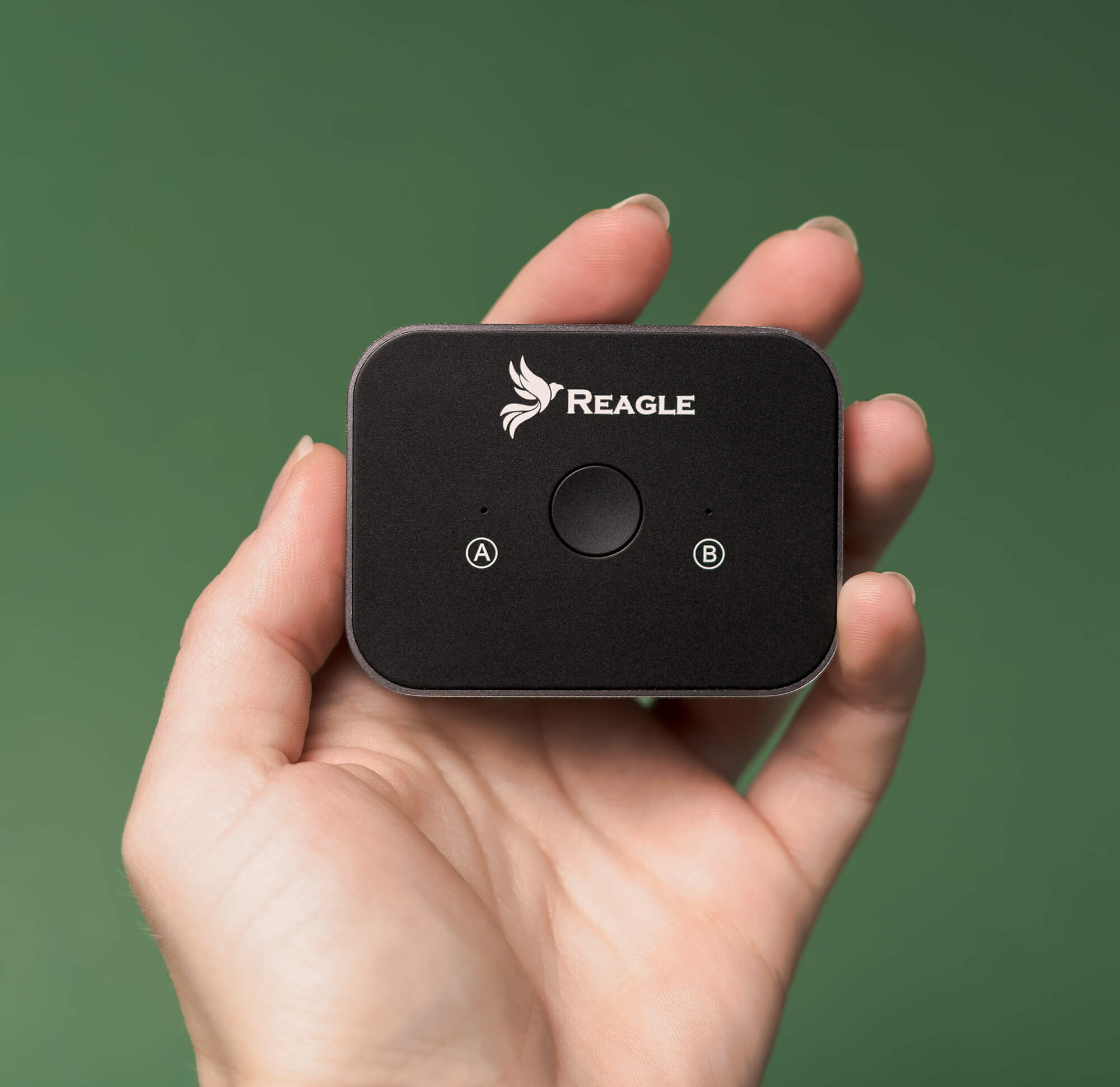 Dłoń trzyma czarne urządzenie Reagle z przyciskiem i punktami A i B na zielonym tle.