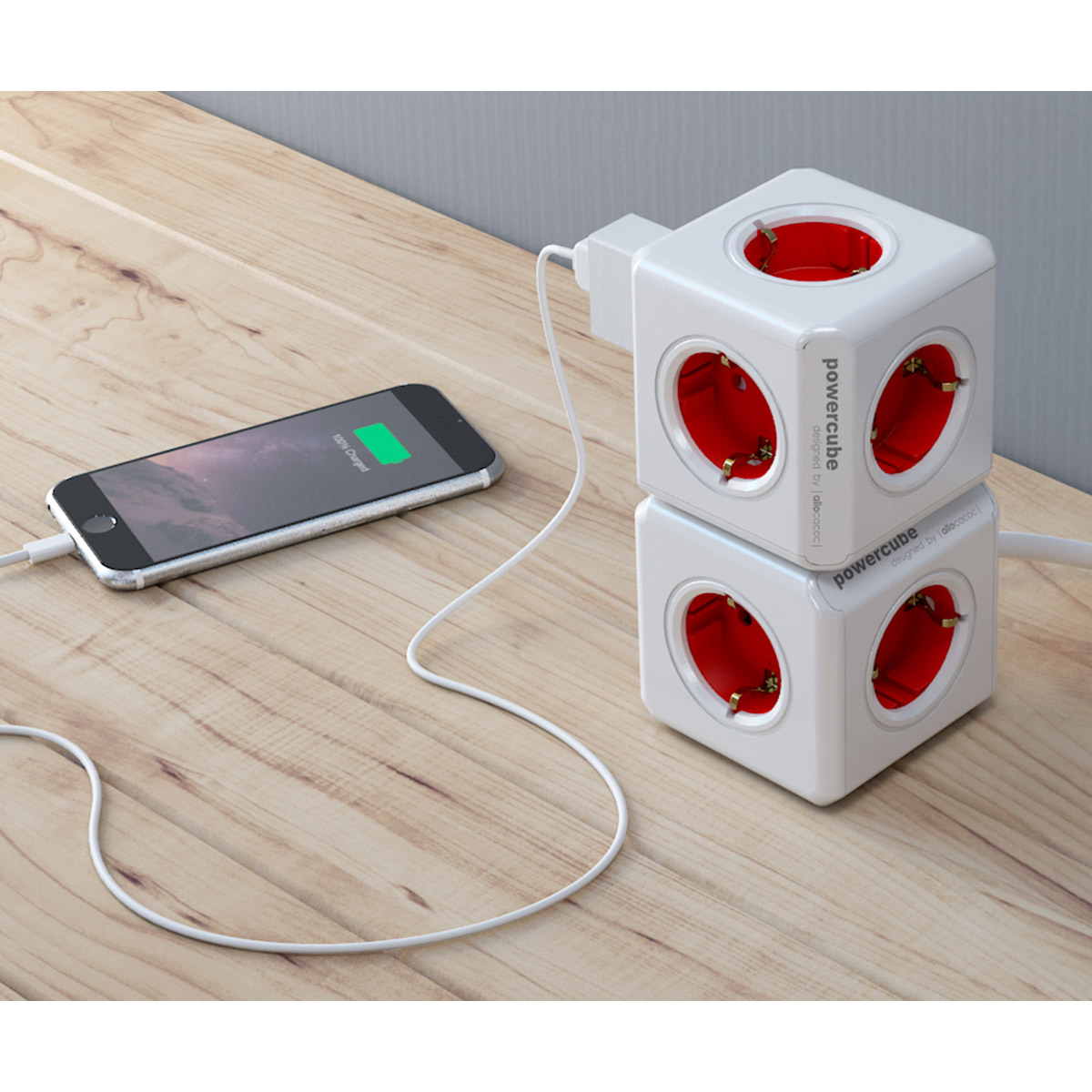 Zwei weiße Power Cube-Steckdosen mit roten Innenräumen, ein Telefon lädt auf einem Holztisch.