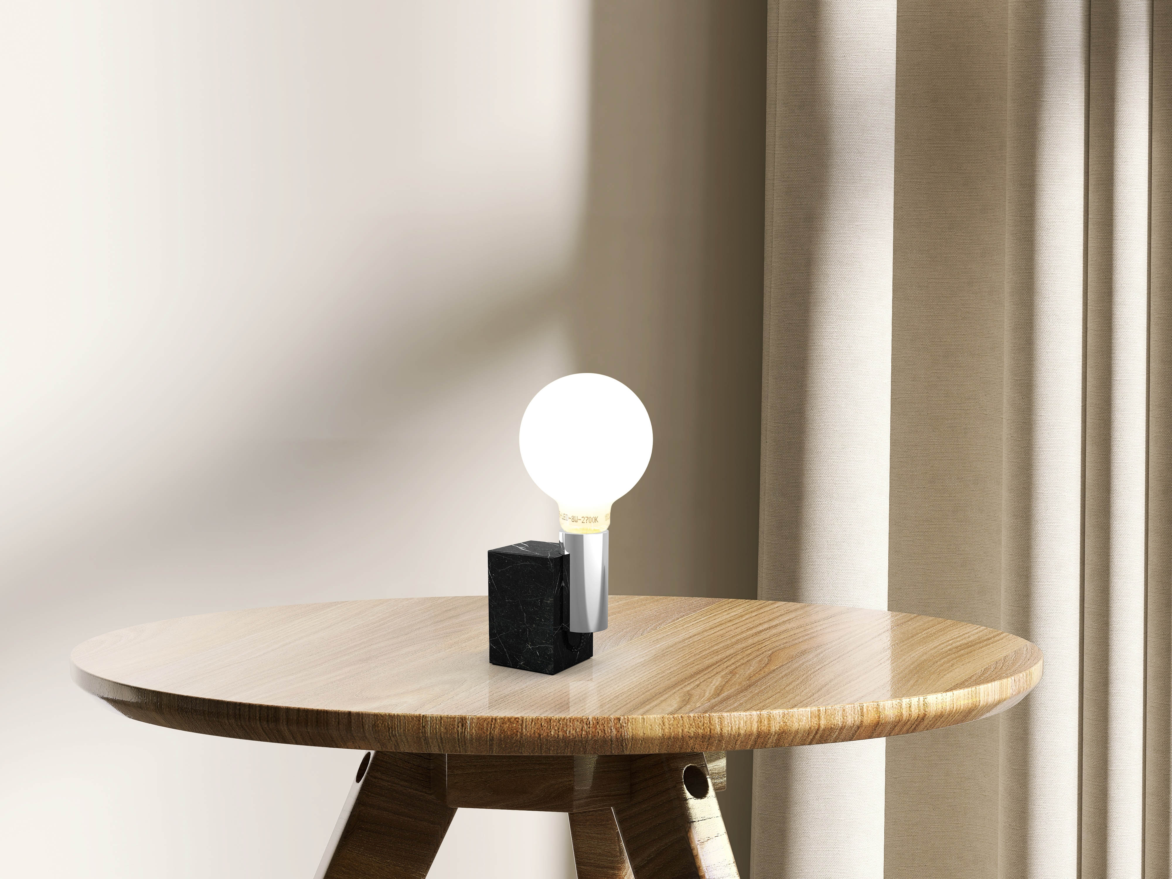 Eine Lampe auf einem Holztisch. Die Lampe hat einen schwarzen Sockel, einen silbernen Stiel und eine weiße Glühbirne.