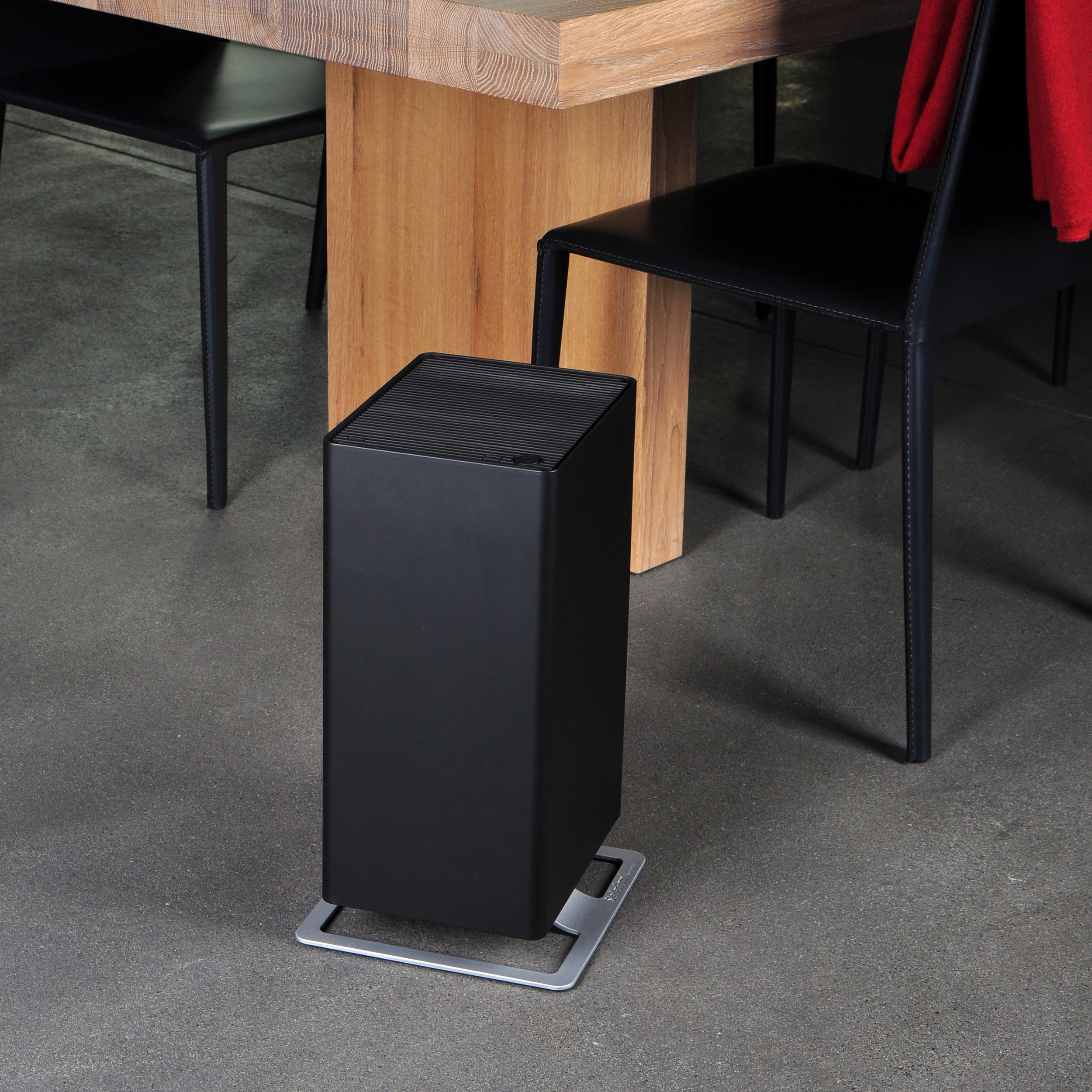 Purificatore d'aria nero su una base di metallo. Un tavolo e sedie in legno sullo sfondo.
