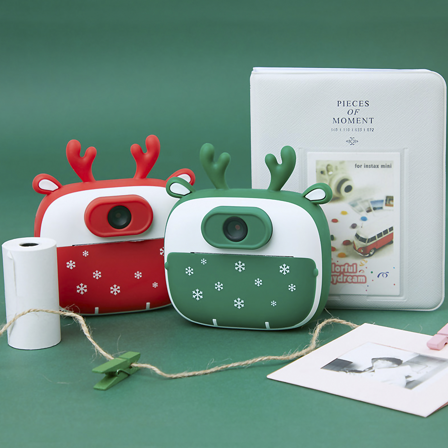Dos cámaras de juguete temáticas navideñas, una roja y otra verde, con un álbum de fotos.