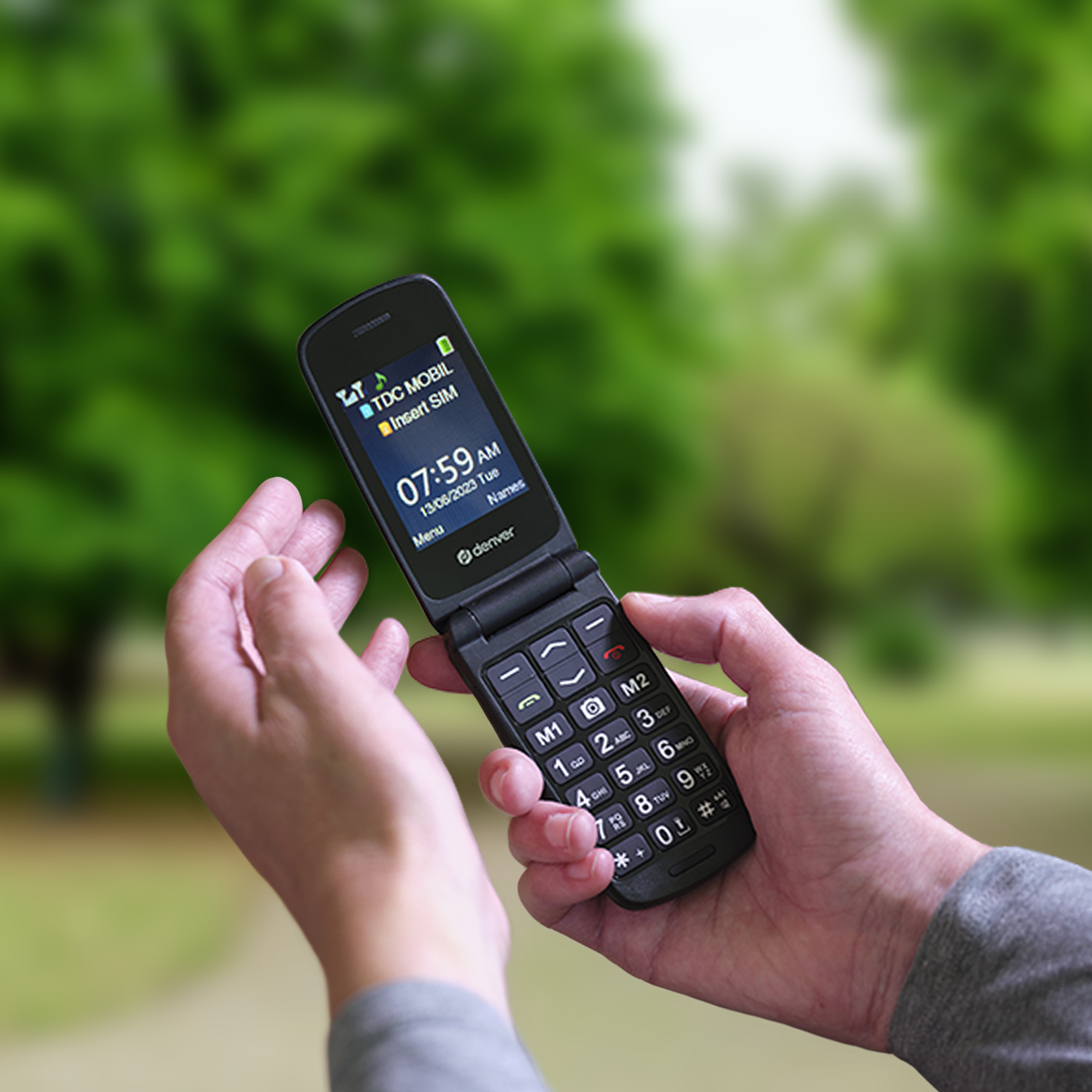 Le mani di una persona che tiene un telefono a conchiglia aperto che mostra l'ora e la data su uno schermo.