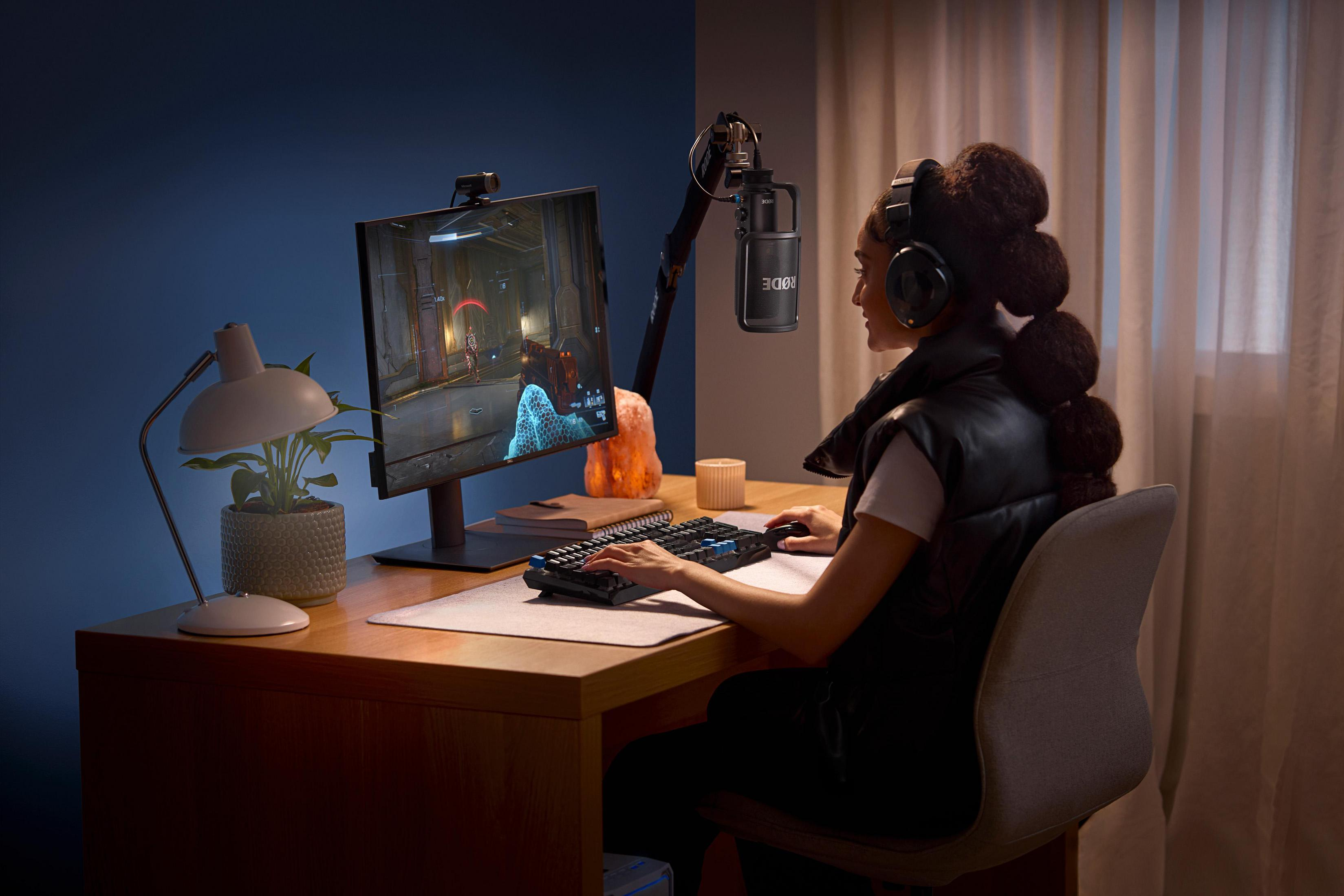 Kobieta grająca z mikrofonem, monitorem, klawiaturą i lampą.