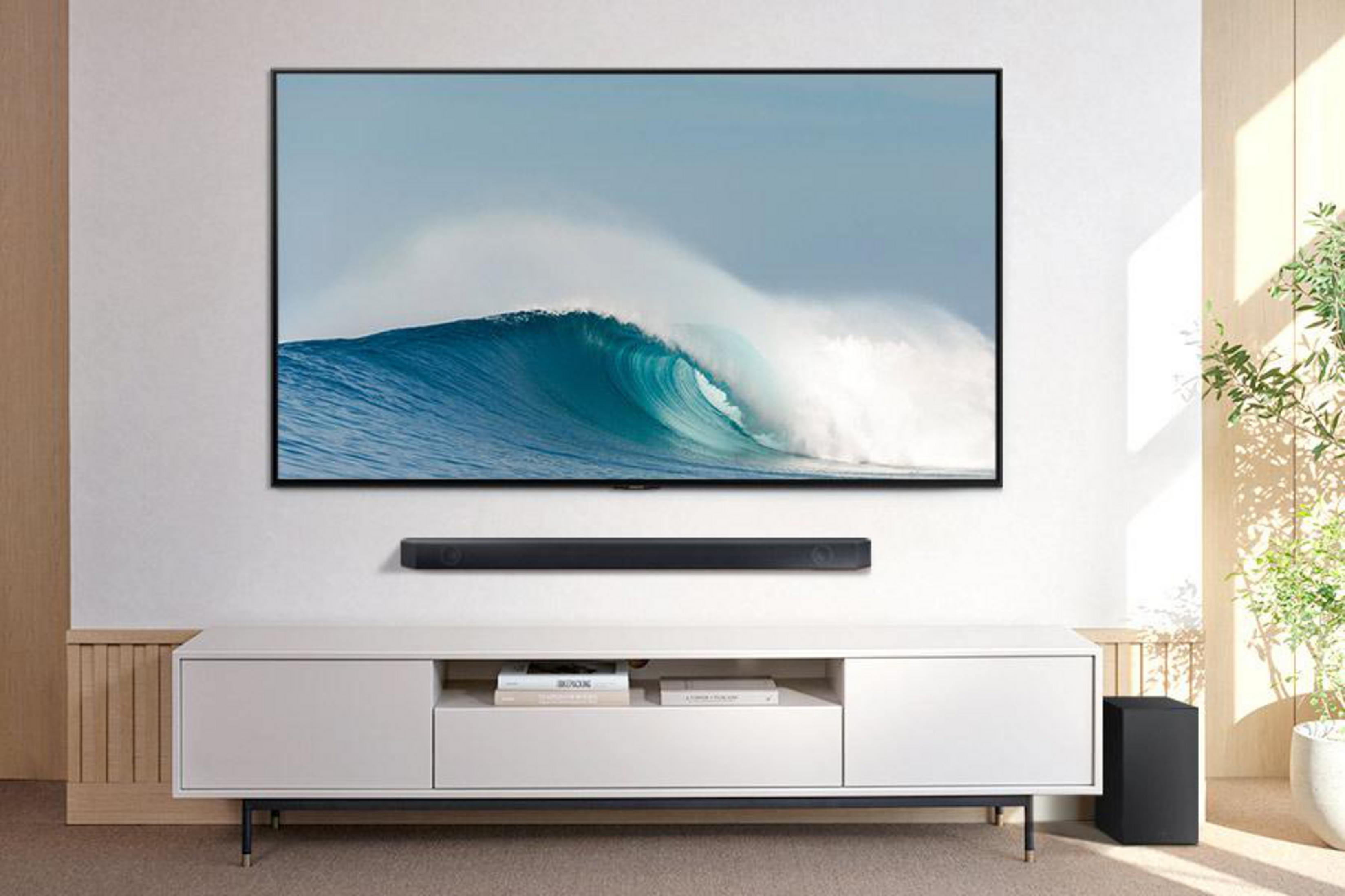 Fernseher an einer weißen Wand. Unter dem Fernseher befindet sich eine Soundbar und rechts ein Subwoofer auf dem Boden.