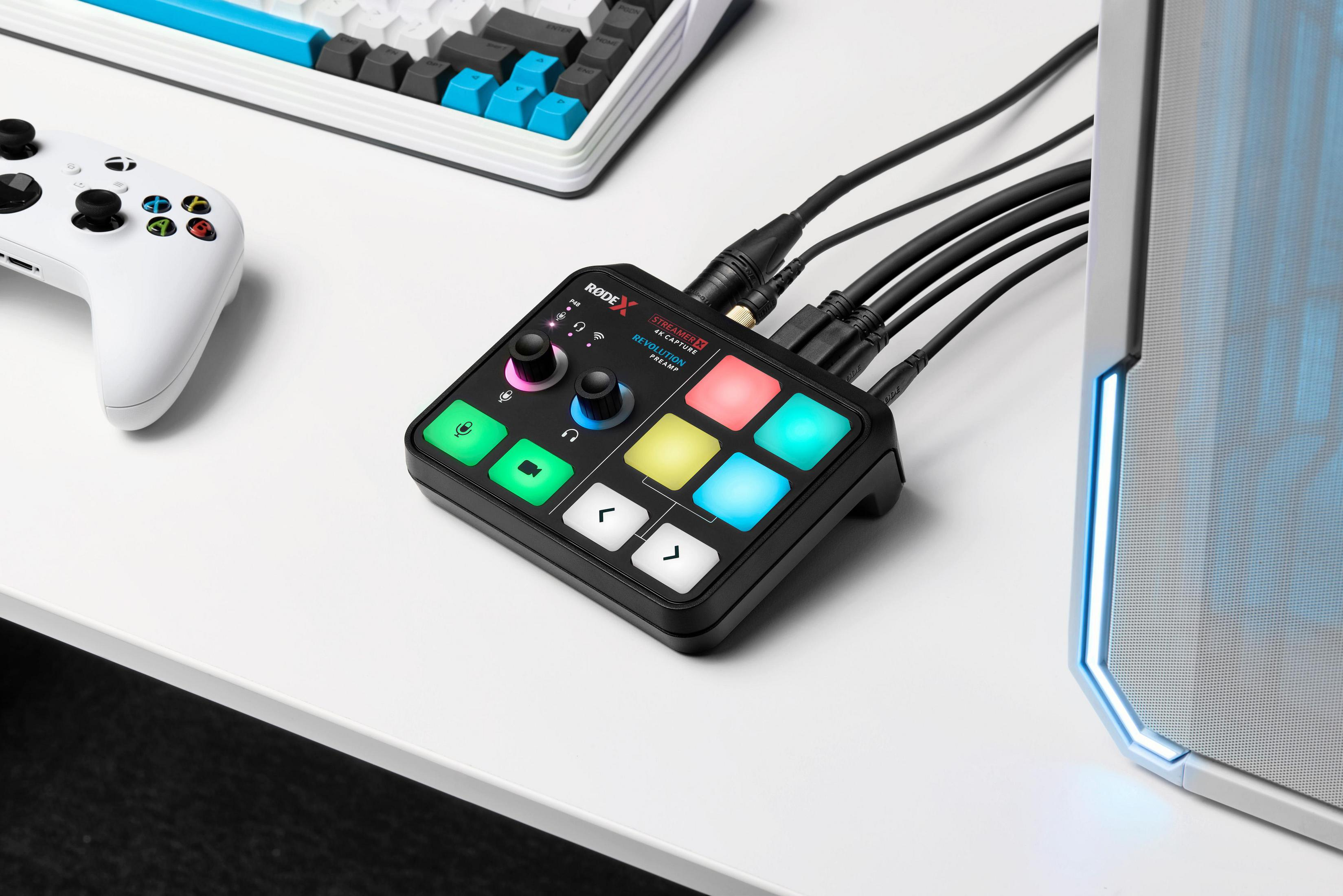 Un mixer audio nero con pulsanti colorati, manopole e cavi collegati su una scrivania bianca.