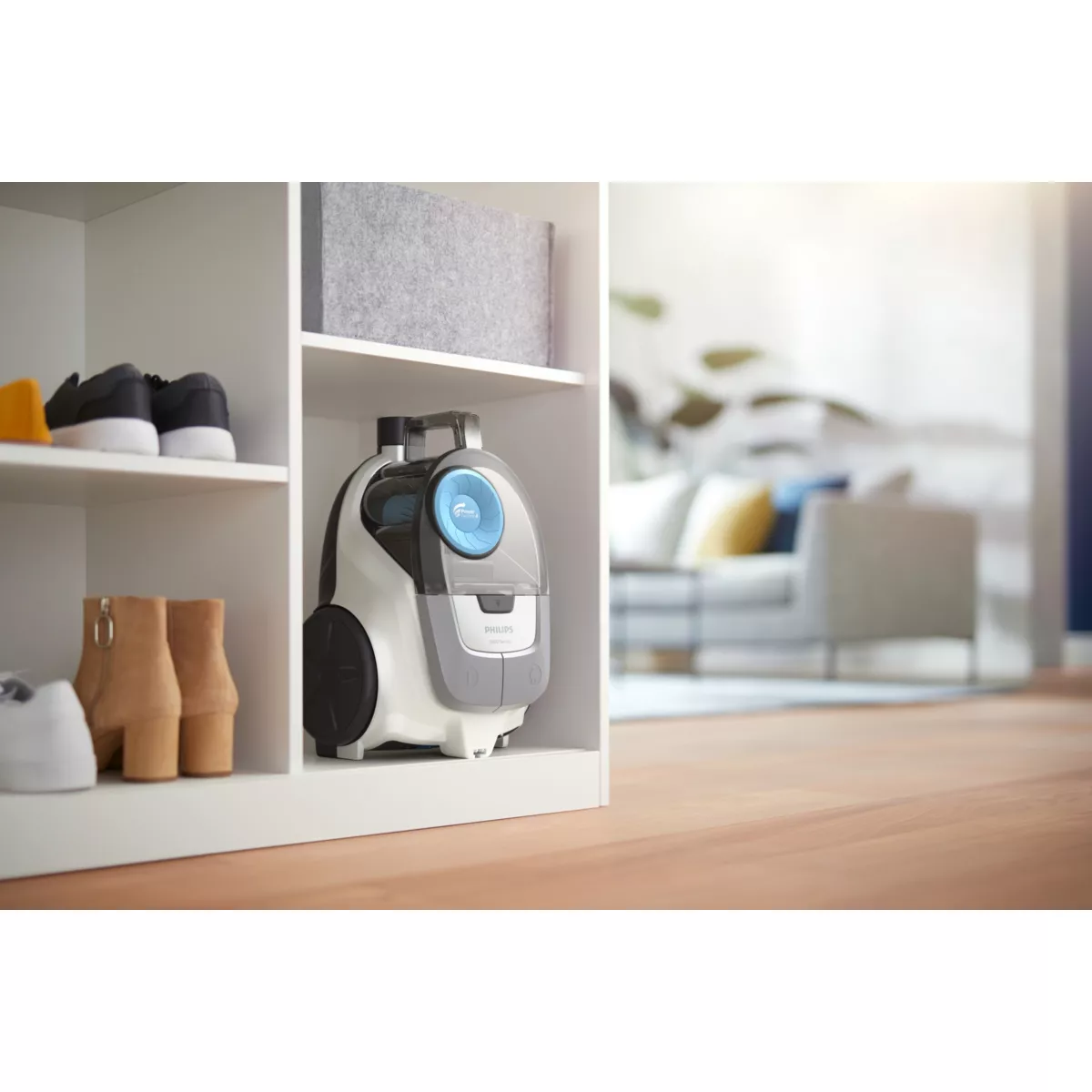 Biały i szary odkurzacz na białej półce, inne przedmioty i rozmyte tło.