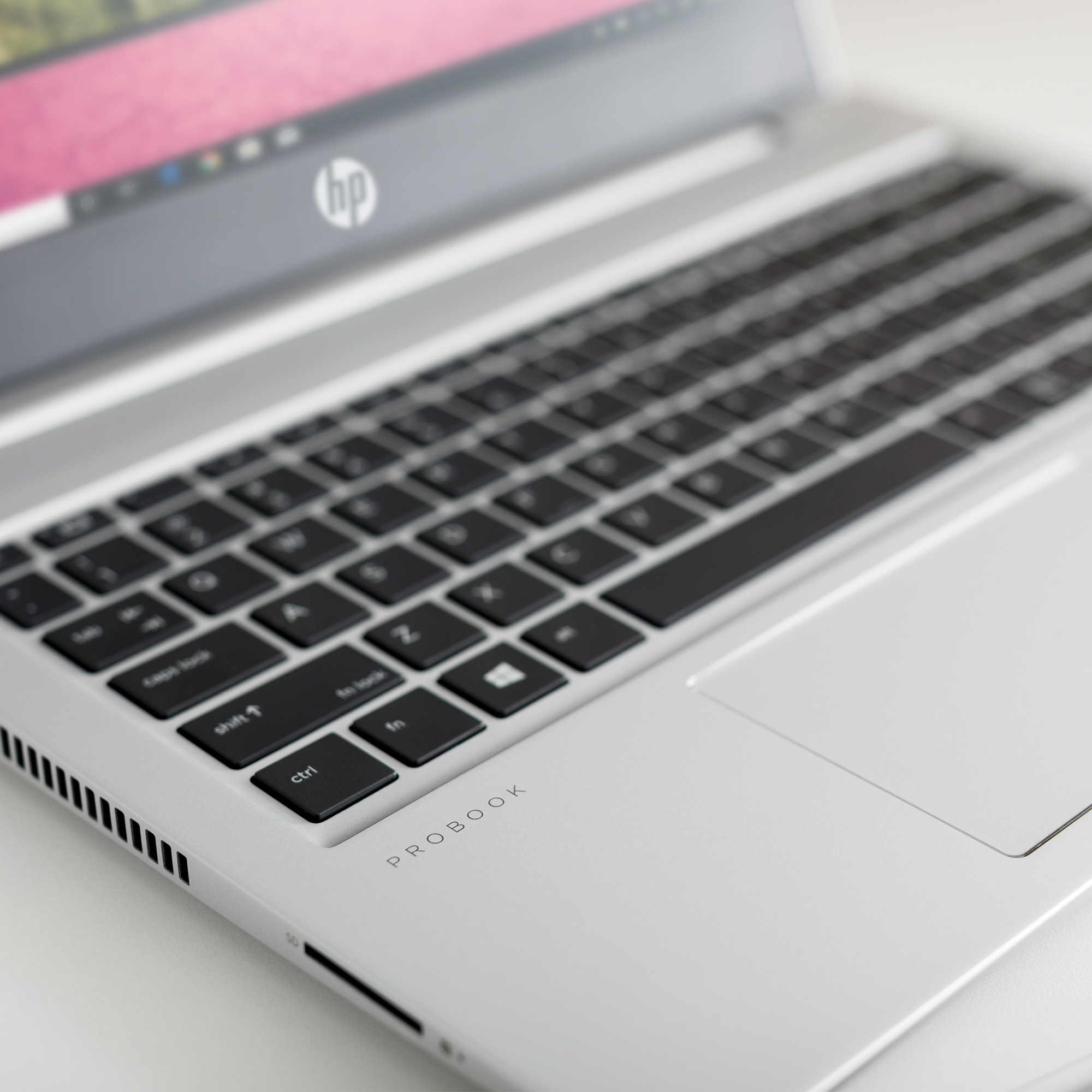 Primo piano di un laptop argentato con tastiera nera e superficie bianca.