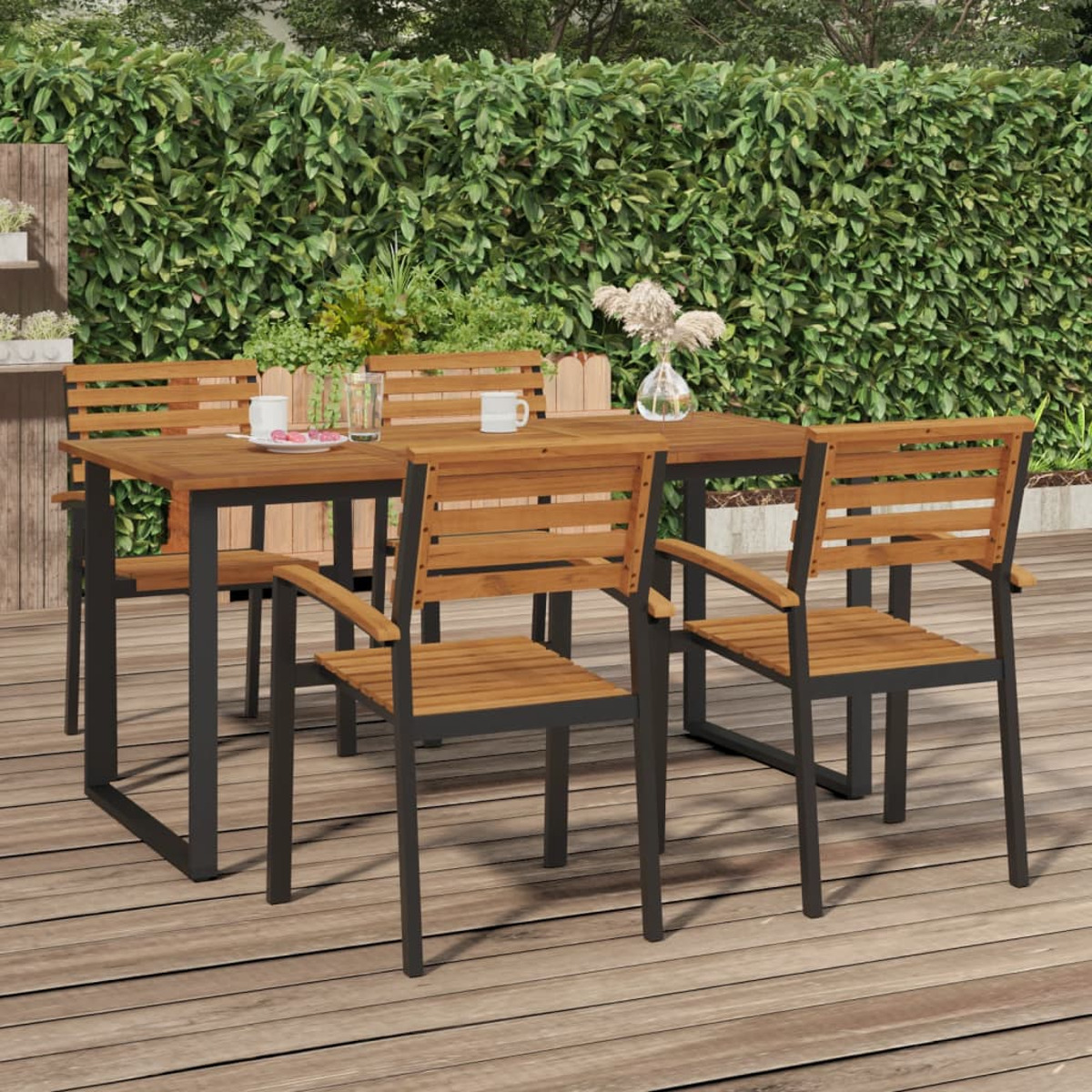 Holztisch mit vier Stühlen. Auf Holzterrasse mit grünem Laub im Hintergrund.