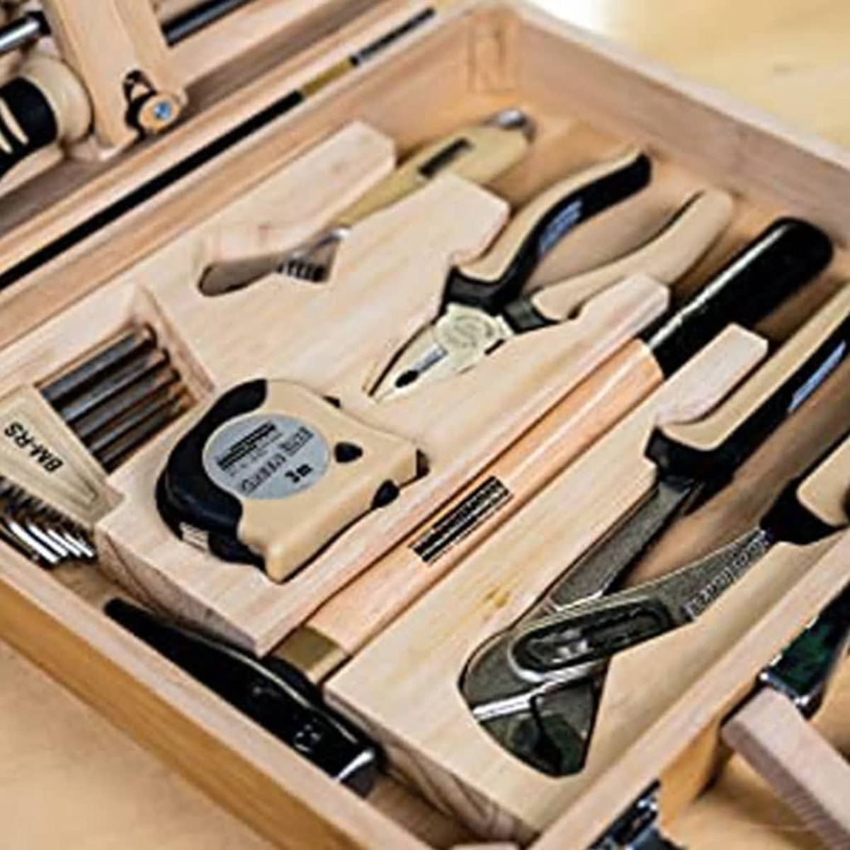 Holzwerkzeugkasten mit verschiedenen Werkzeugen, darunter Zangen, Hammer und Maßband.