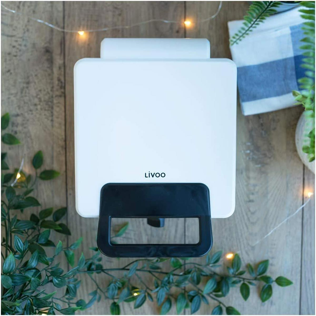 Białe gofrownica z czarnym uchwytem. Drewniany stół i niebiesko-biały ręcznik. Widok z góry.