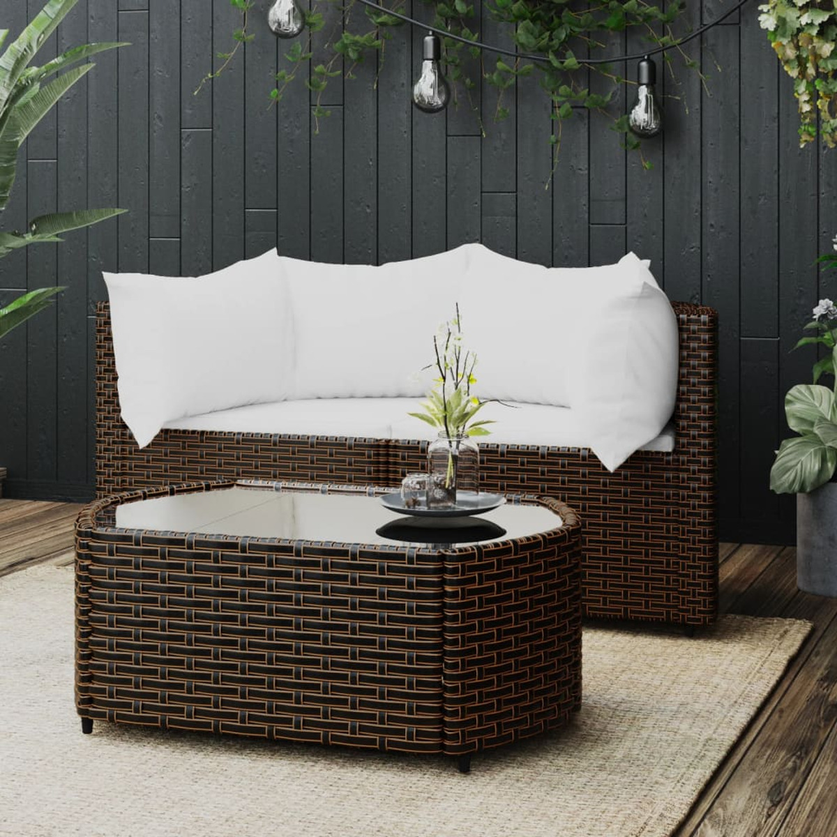 Szene im Freien: Sofa, Couchtisch, Teppich, Pflanzen und Lichterkette vor schwarzer Wand.