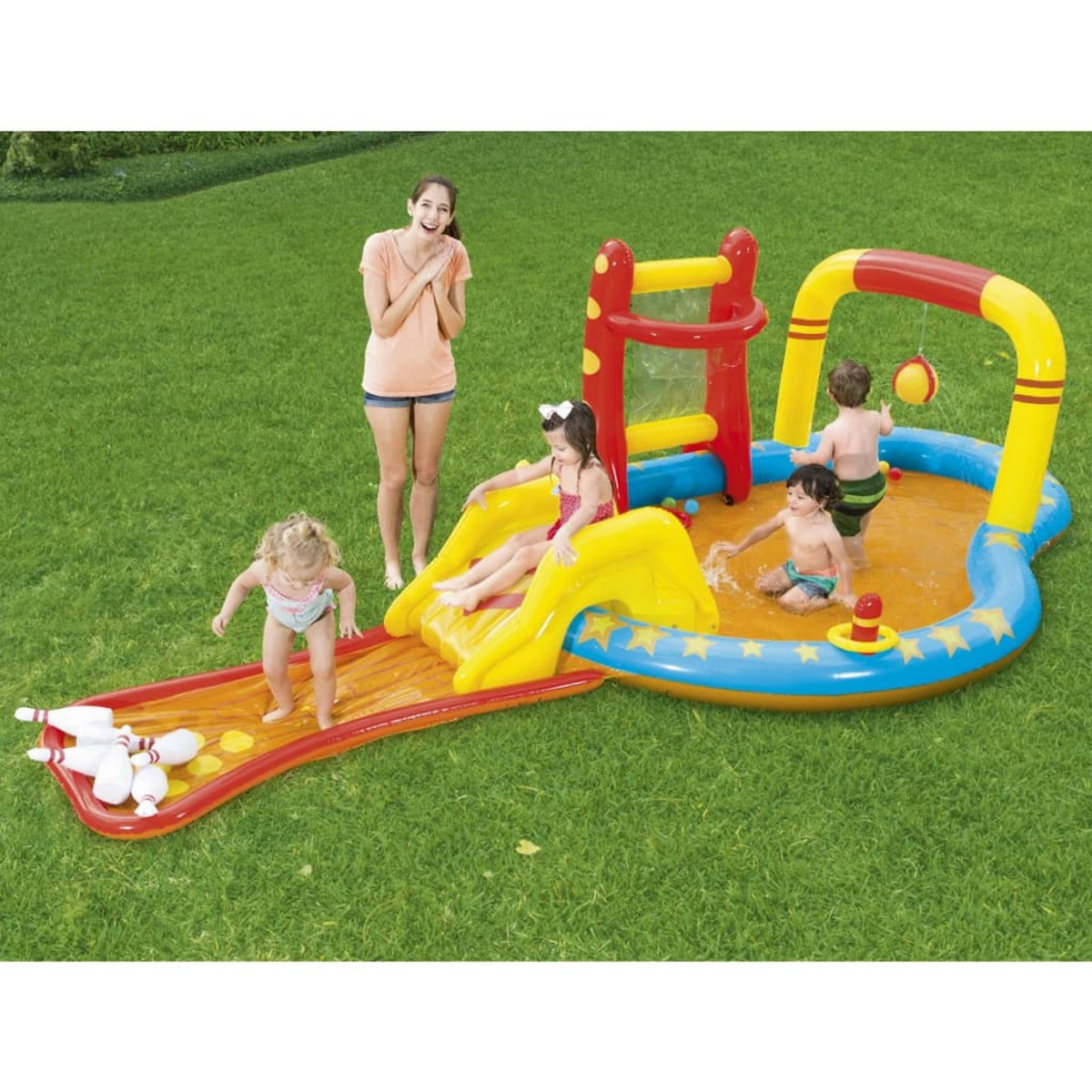 Niños jugando en una piscina con tobogán, bolos y red. Una mujer está cerca.
