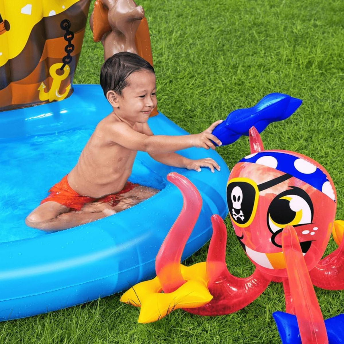 Un bambino in piscina che gioca con un polpo giocattolo, con decorazioni a tema nave pirata sullo sfondo.