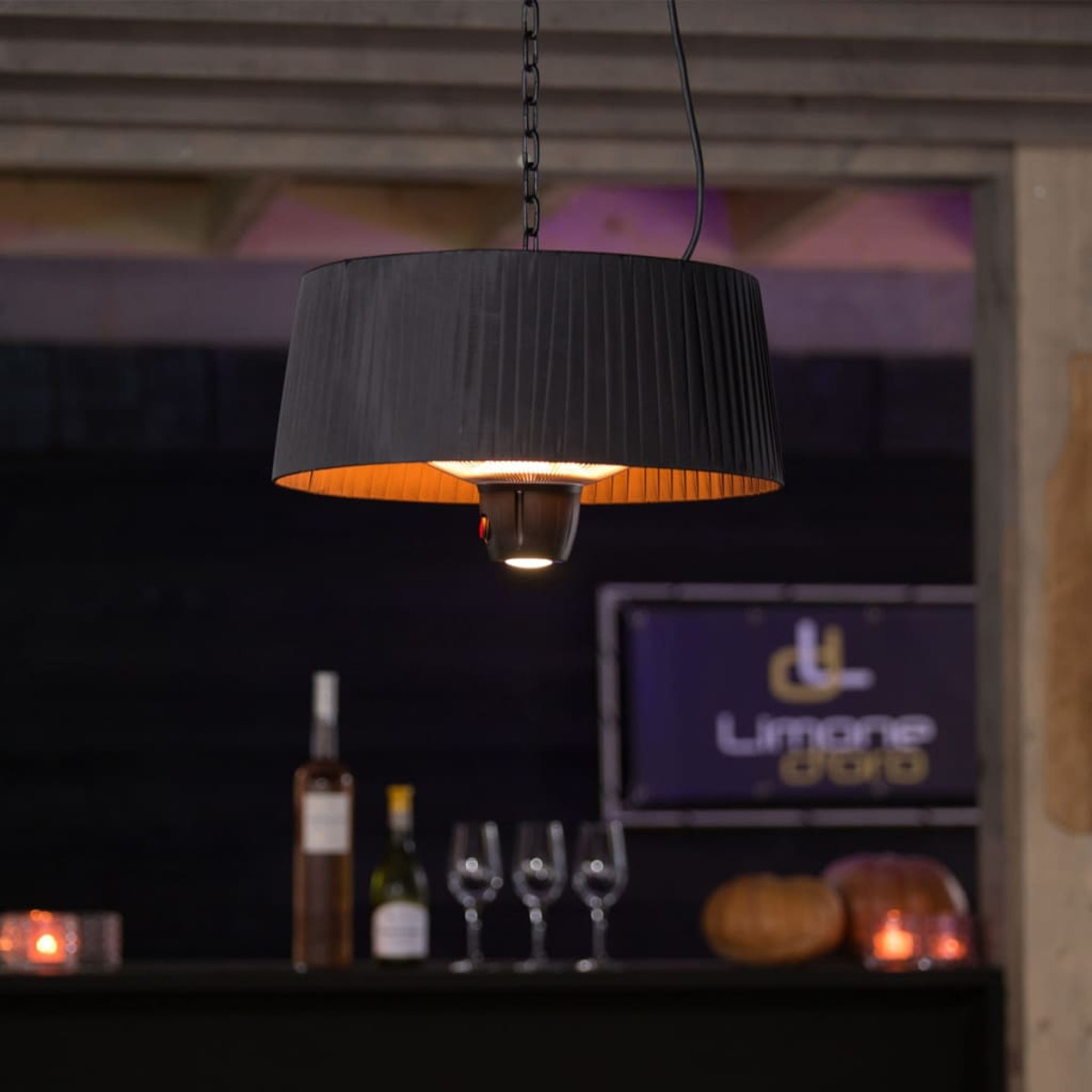 Zwarte hanglamp voor buiten met gouden binnenkant, boven een bar met flessen.
