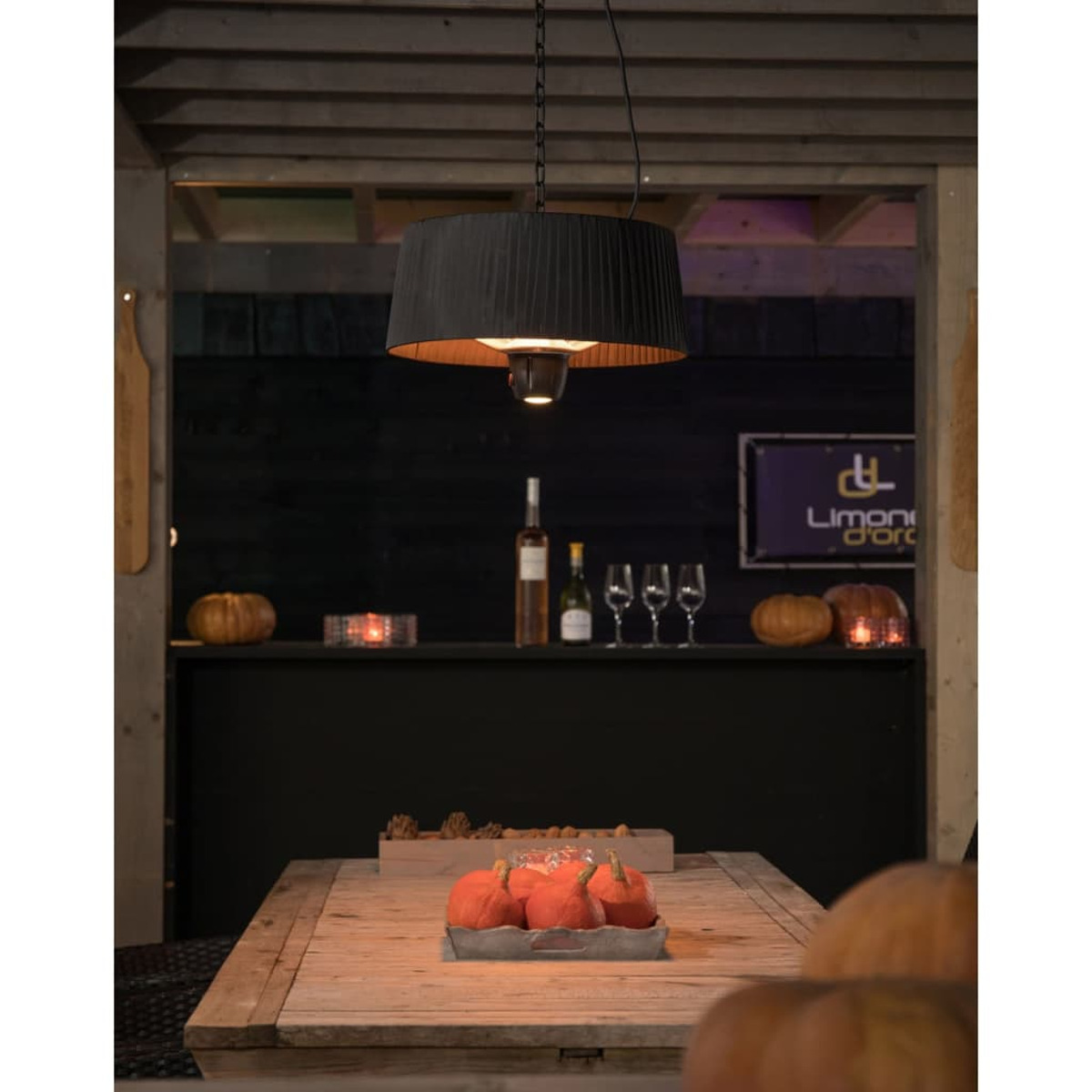 Buitenscène met een tafel en hanglamp, pompoenen en wijnflessen zijn aanwezig.