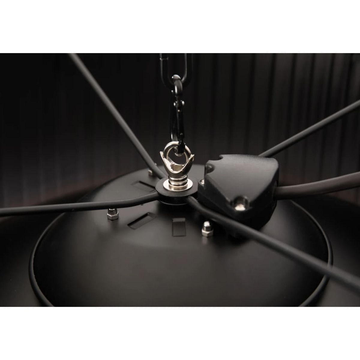 Detail van een zwarte plafondlamp. Kettingen, draden en een centraal onderdeel. Zwart en zilver.