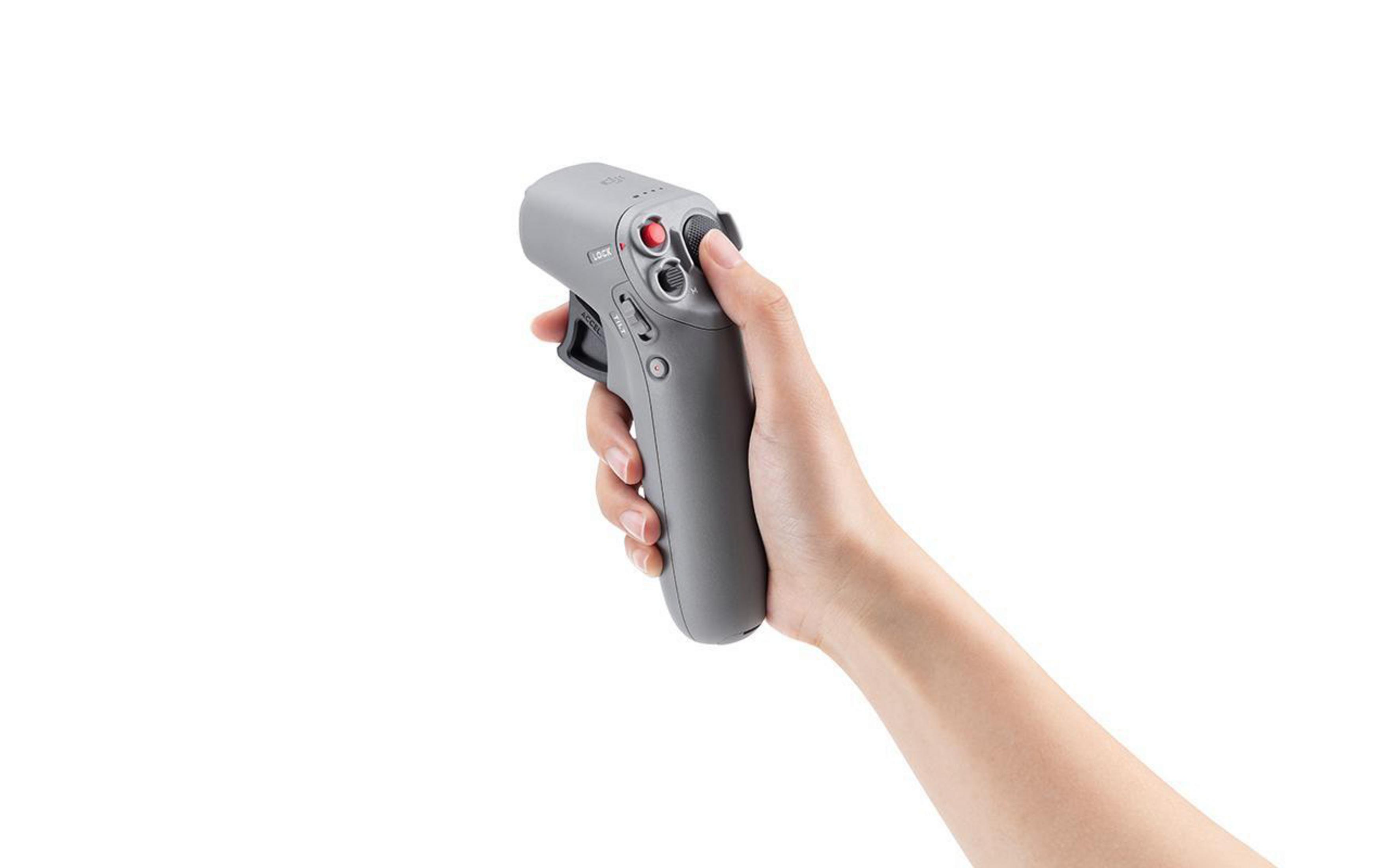Ręka trzyma szary kontroler drona z czerwonymi i czarnymi przyciskami, na białym tle.