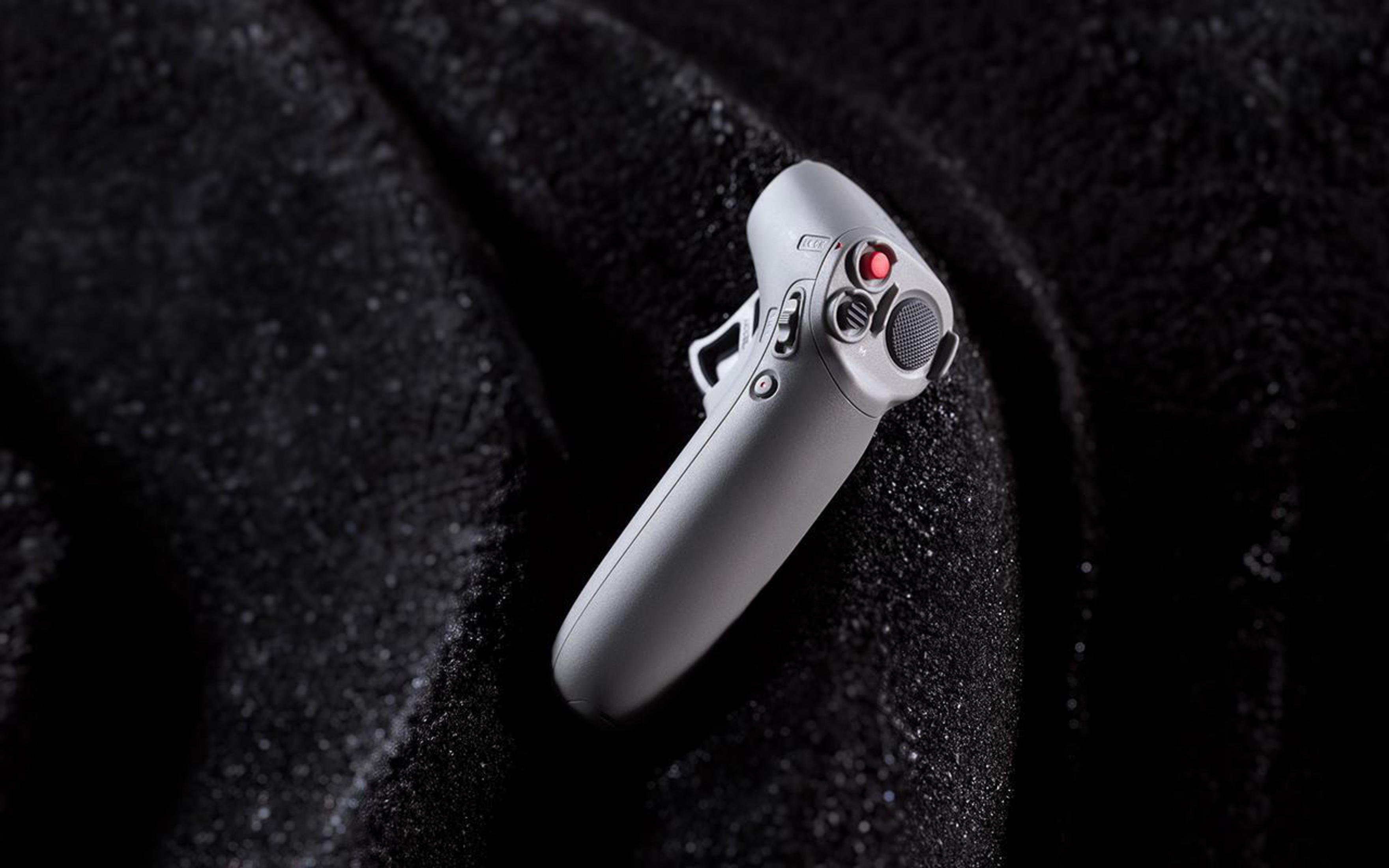 Szary kontroler drona na czarnej, teksturowanej powierzchni. Ma przyciski, ekran i czerwony przycisk.