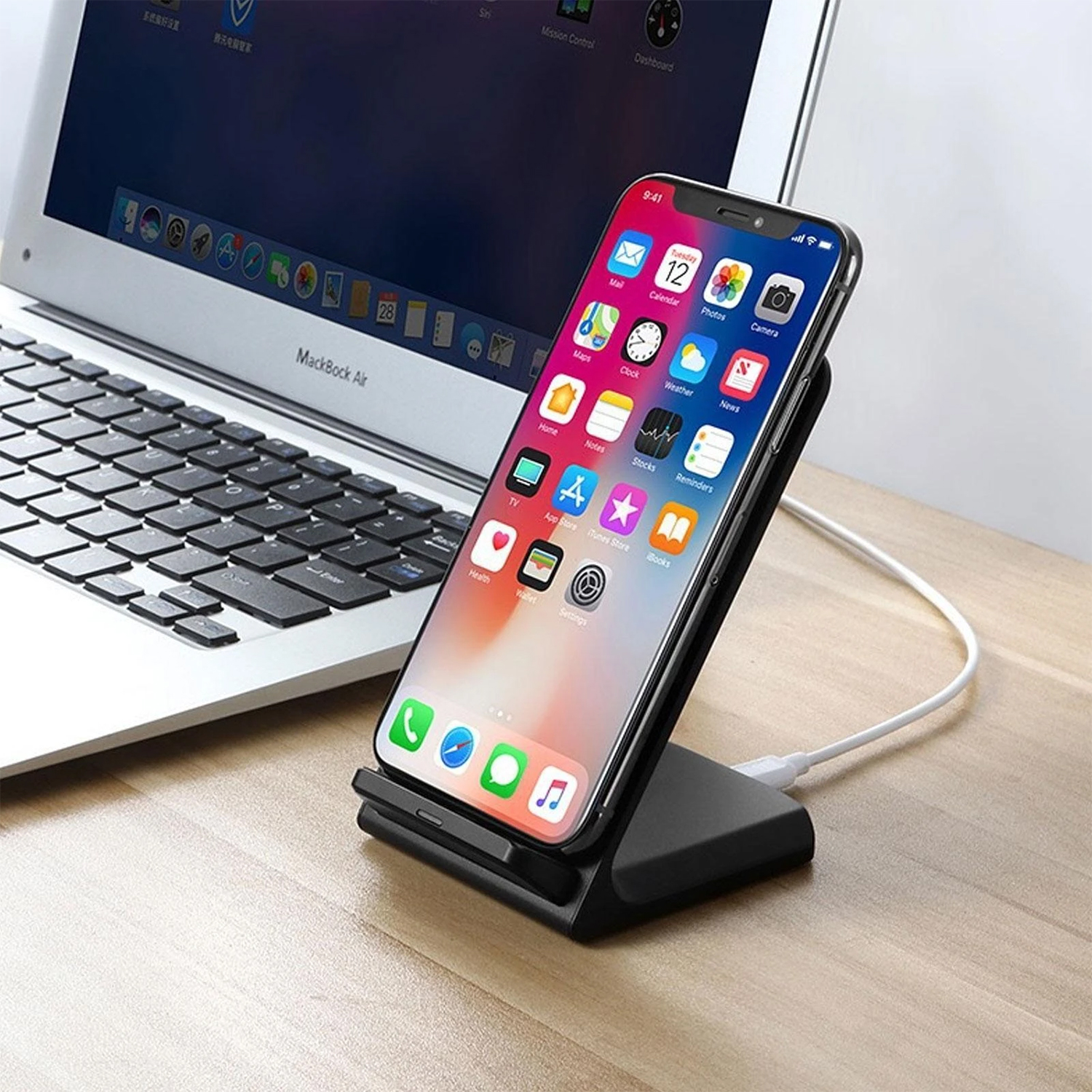 Un telefono si sta caricando su un supporto nero vicino a un laptop su una superficie di legno.