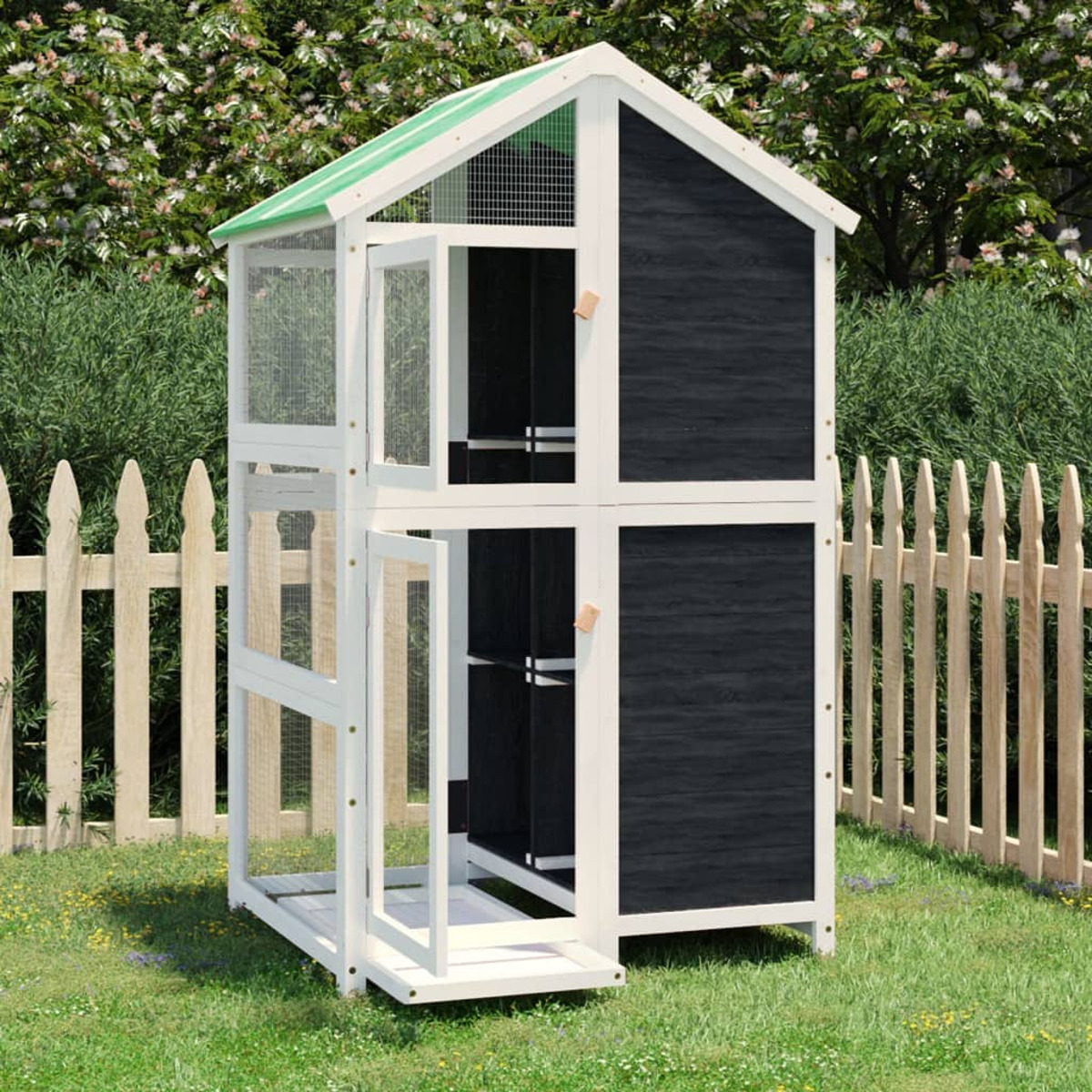 Ein weißes und schwarzes Katzenhaus mit offenen Türen, auf einer Wiese mit Zaun.