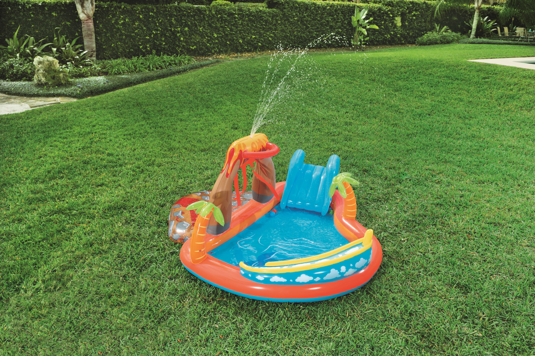 Kolorowy park wodny z wulkanem, zjeżdżalnią i basenem na zielonej trawie.