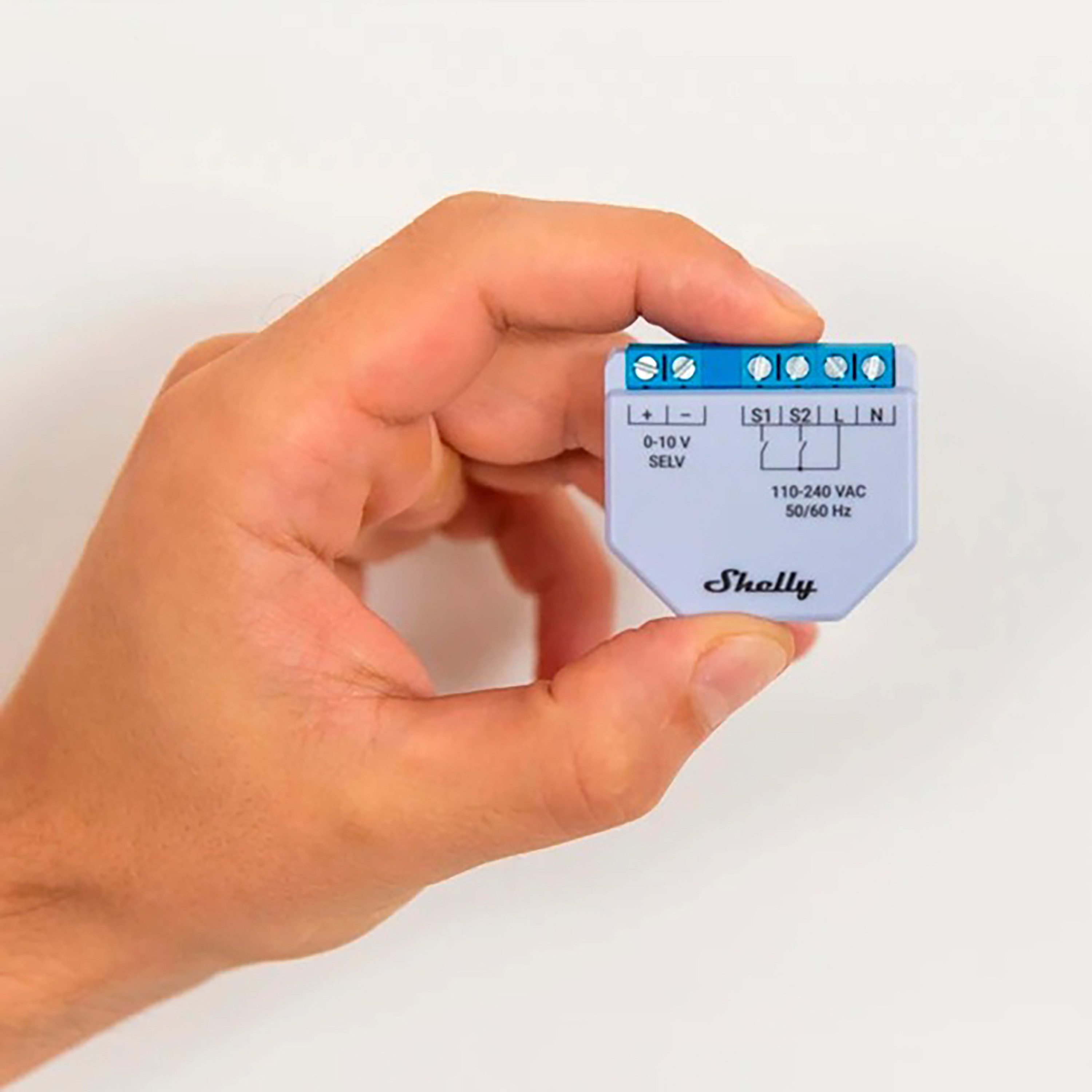Una mano sosteniendo un pequeño dispositivo doméstico inteligente gris claro con terminales azules.