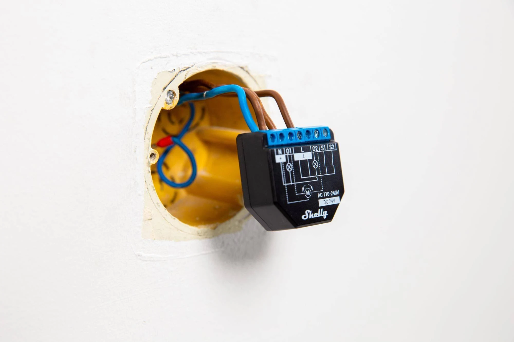 Un interruttore intelligente nero installato in una presa a muro, con fili collegati. Lo sfondo è un muro bianco.