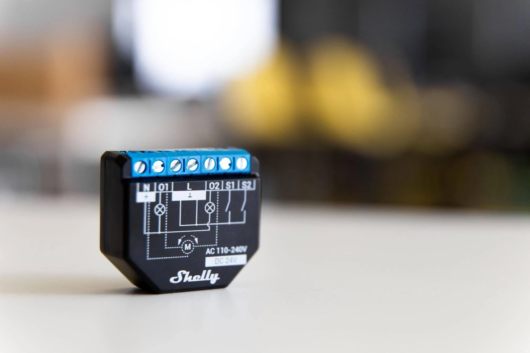 Un dispositivo smart home Shelly nero con morsetti blu, etichettato con vari simboli elettrici.