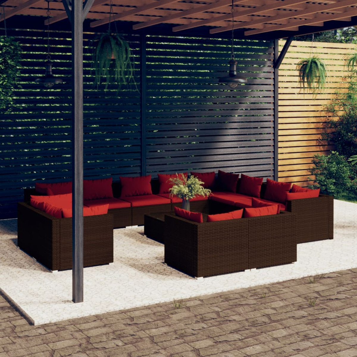 Braunes Outdoor-Wicker-Sofa-Set mit roten Kissen auf einer Terrasse. Pergola und Pflanzen im Hintergrund.