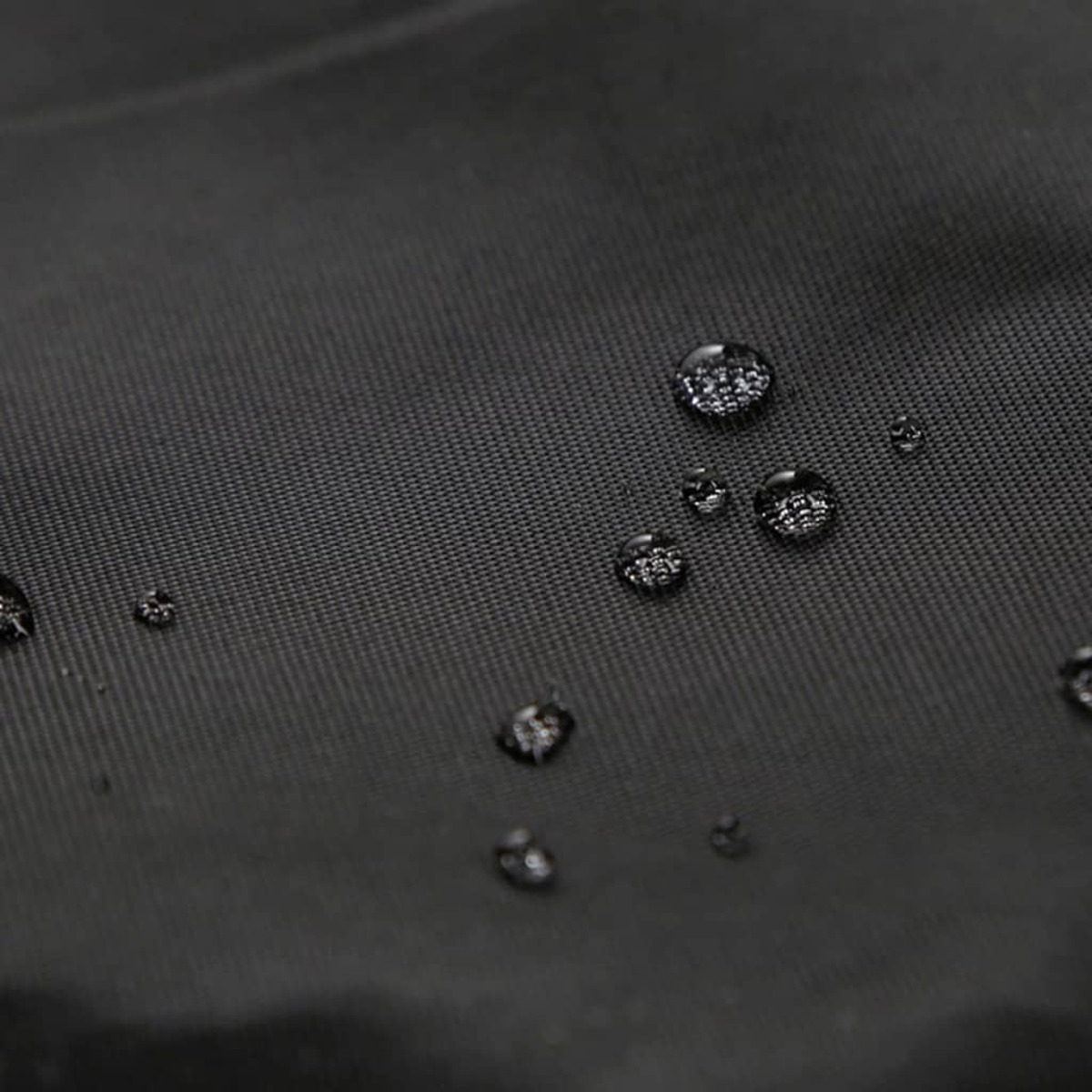 Schwarzer Stoff mit Wassertropfen. Die Tropfen sind klar und reflektierend.