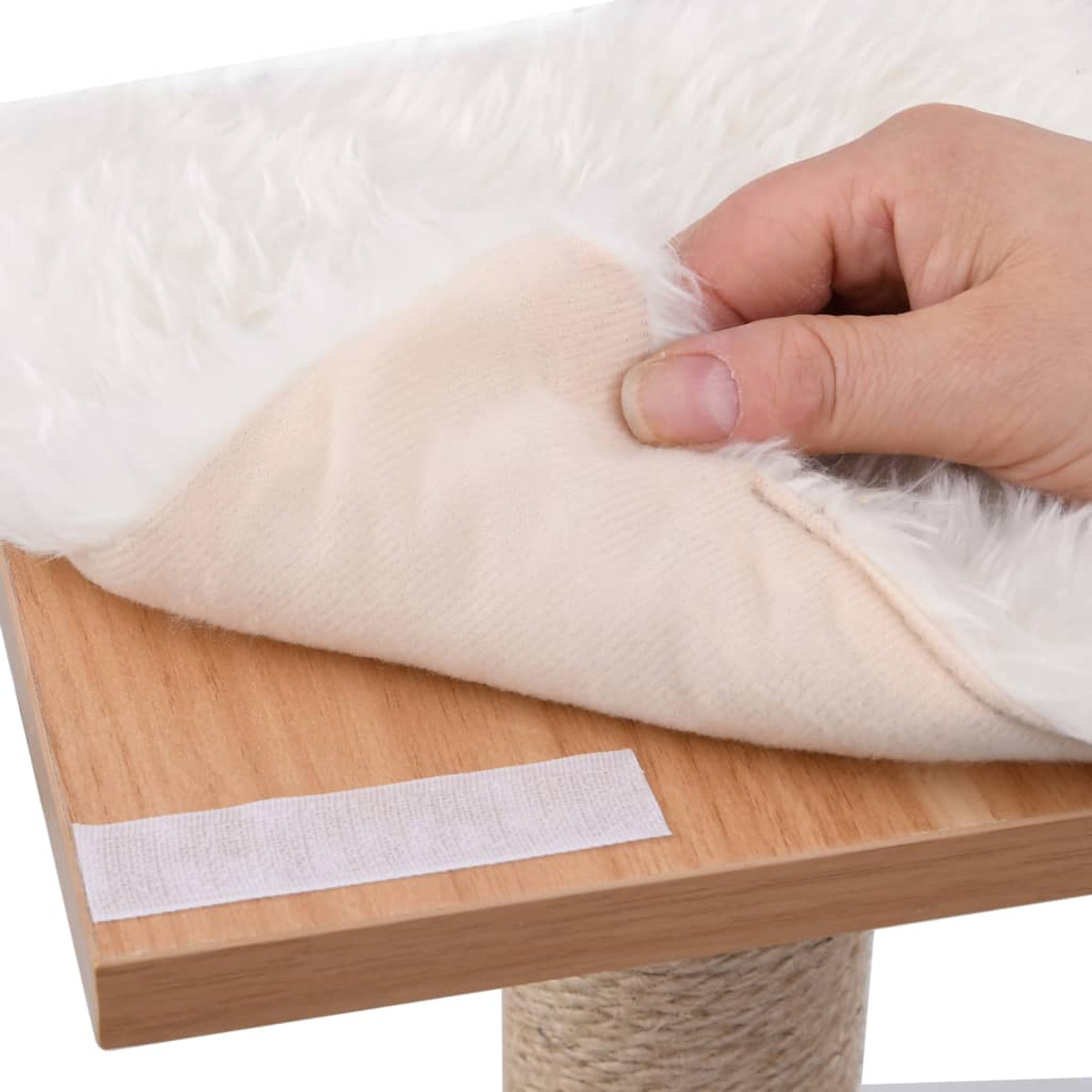 Hand hält einen flauschigen weißen Katzenbett-Einsatz, Klettstreifen auf Holz.
