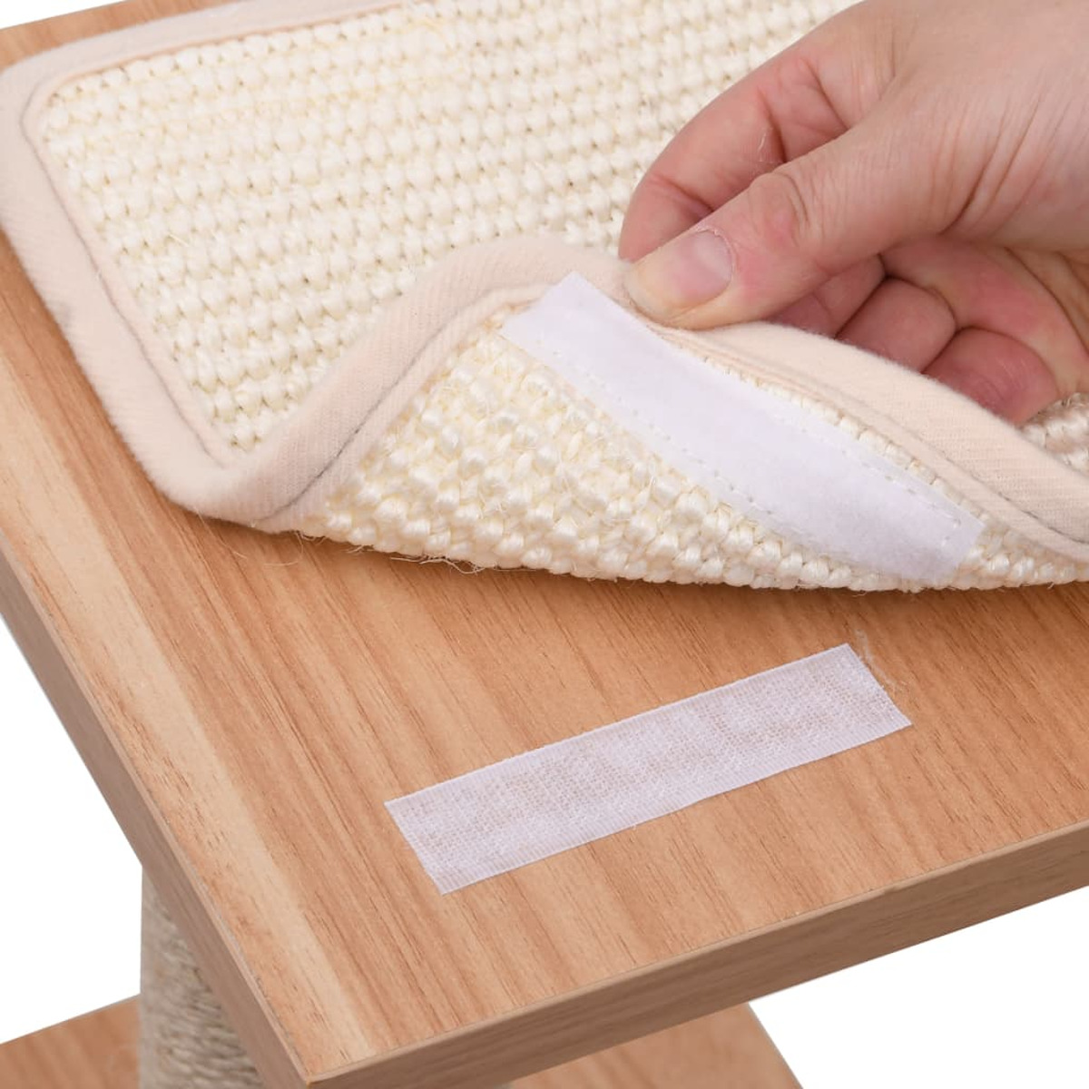 Eine Hand befestigt einen Klettstreifen an einem Katzenkratzbaum. Beige, Holzstruktur.