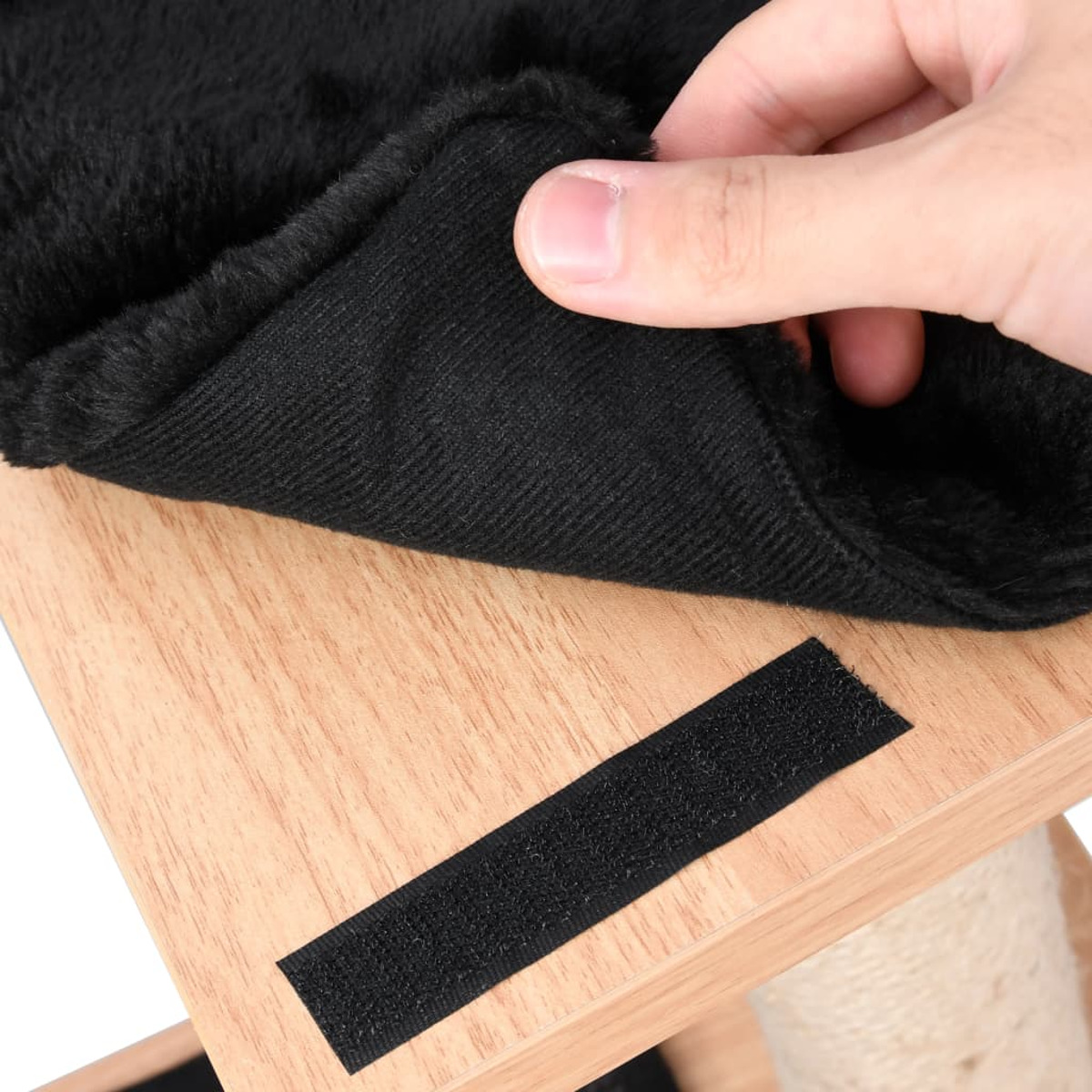 Hand hält einen schwarzen Stoff über einer Holzoberfläche mit Klettverschluss.