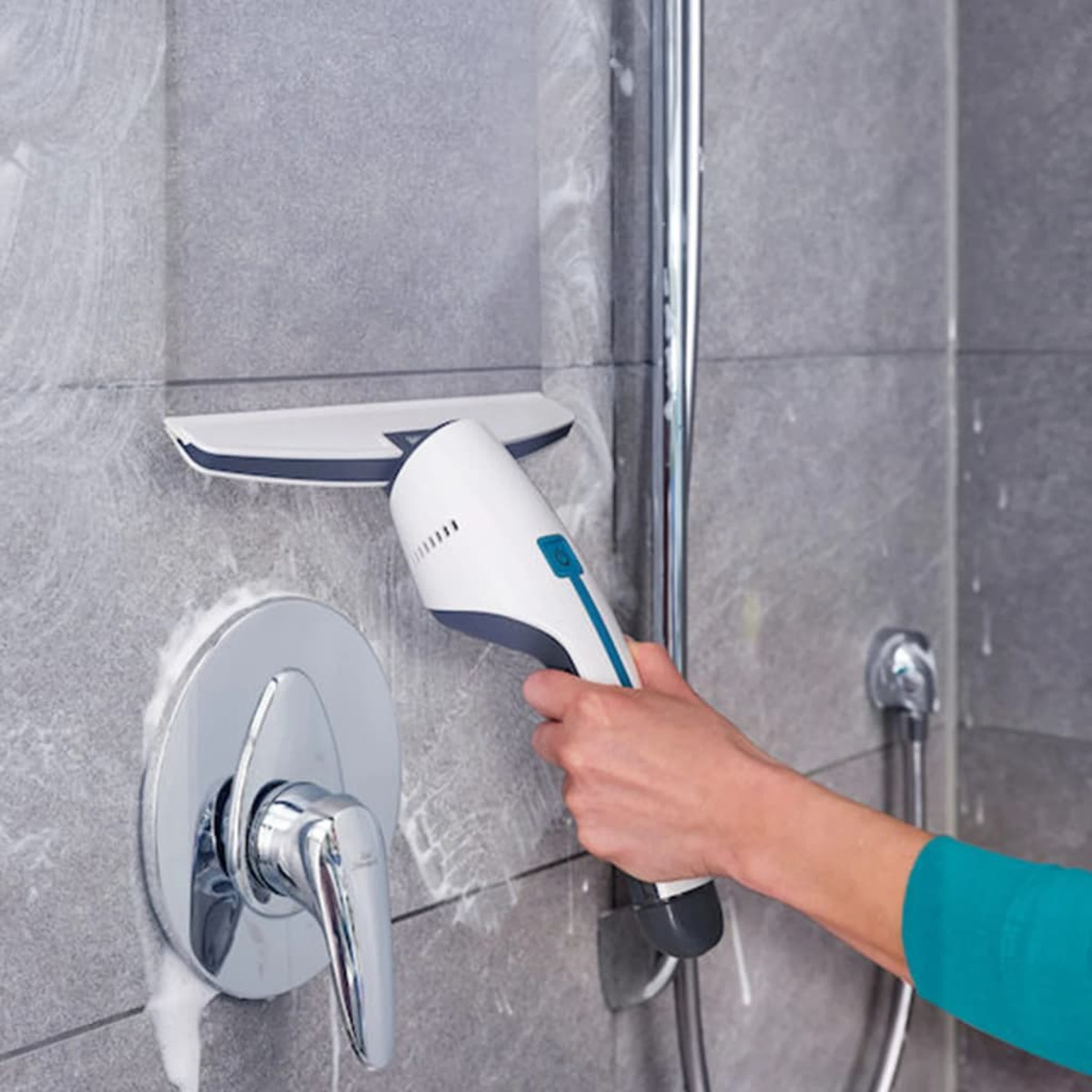 Osoba czyszcząca szarą, kafelkową ścianę prysznica za pomocą białego i szarego narzędzia czyszczącego.