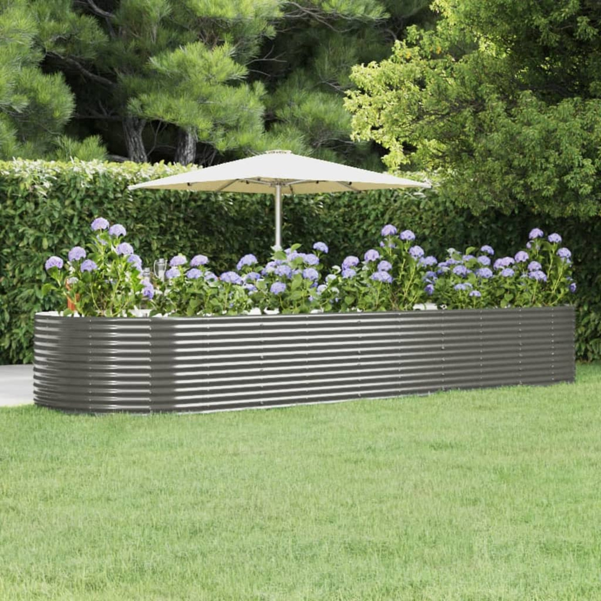 Erhöhtes Gartenbeet aus Metall mit lila Blumen und einem weißen Regenschirm. Grünes Gras und Büsche.