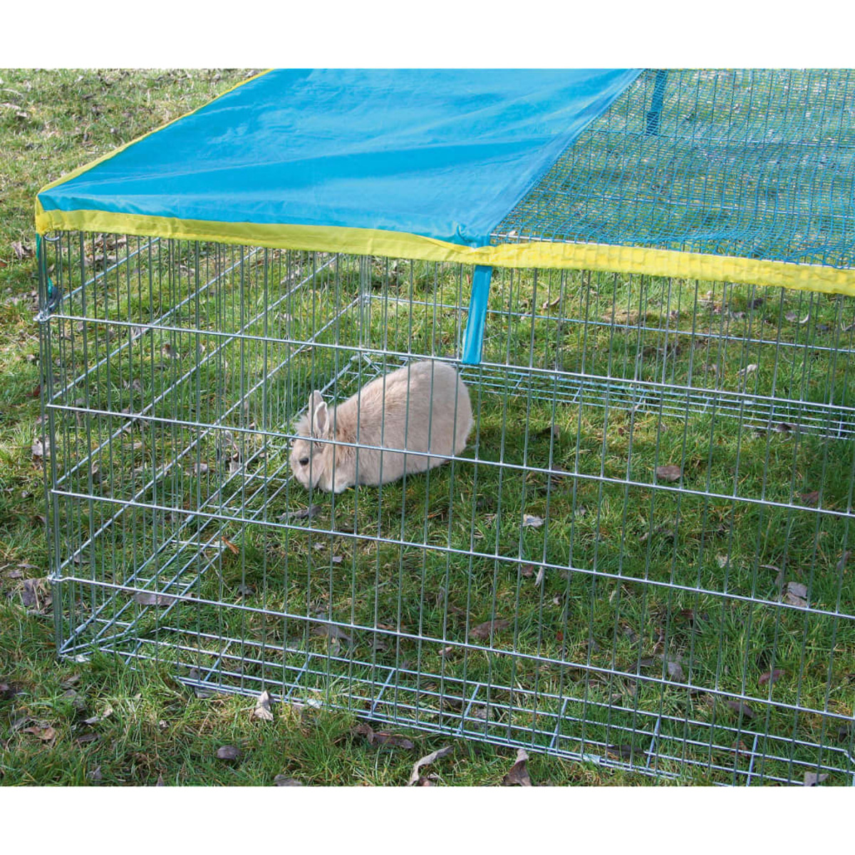 Ein Kaninchen in einem Drahtkäfig mit blauem und gelbem Dach. Der Käfig steht im grünen Gras.