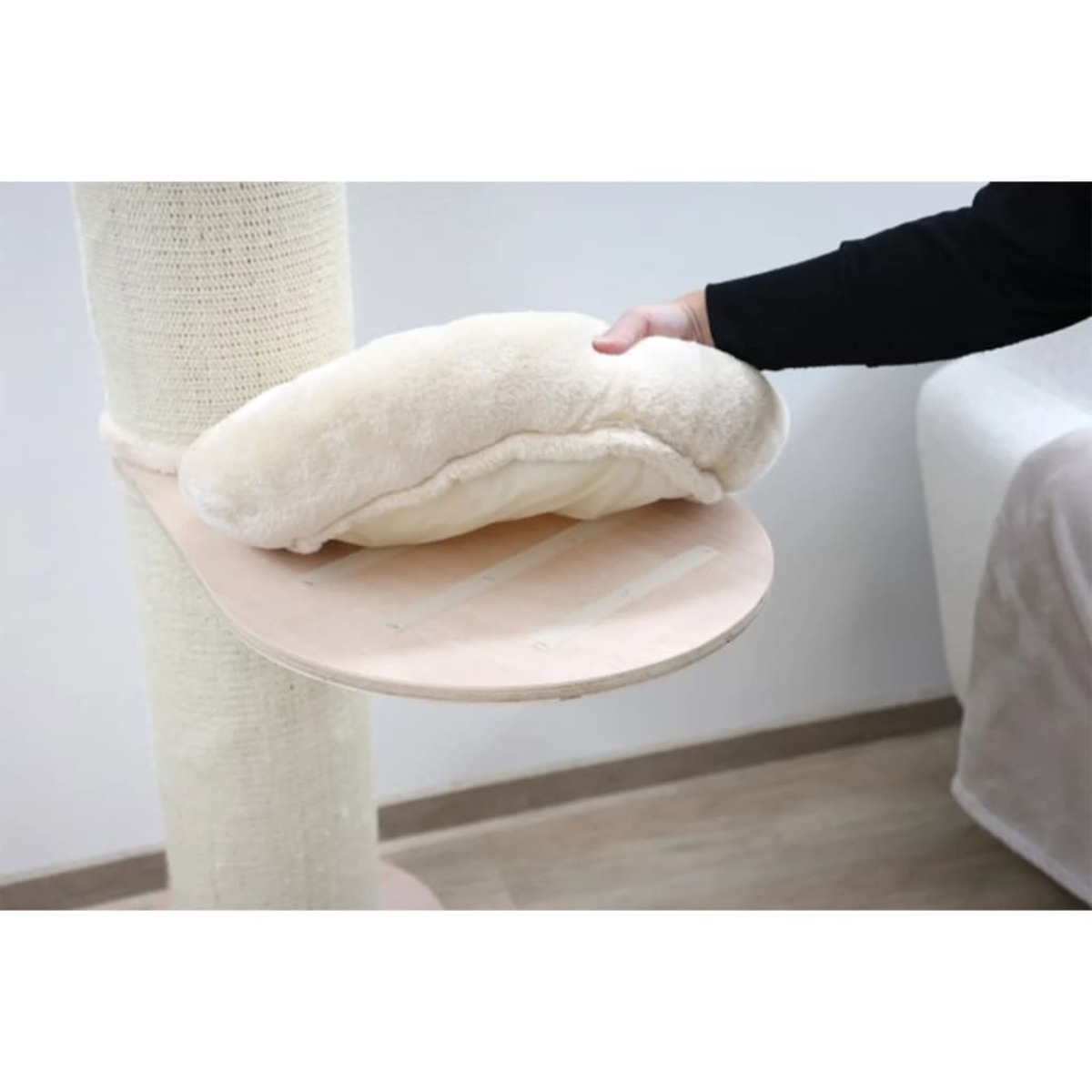 Hand legt weißes Kissen auf eine Plattform des Katzenbaums. Plattform aus hellem Holz.