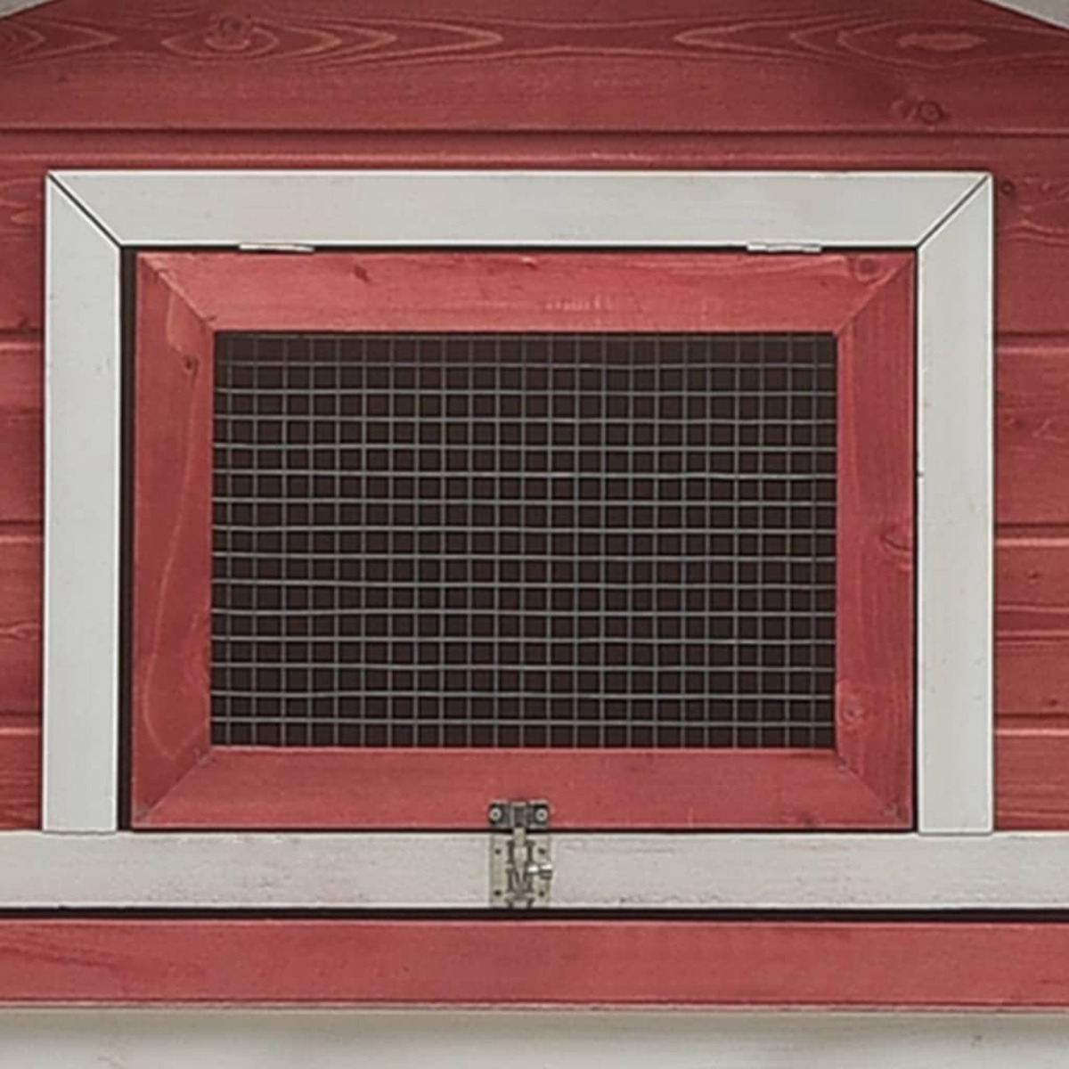 Rotes Holzfenster mit einem Drahtgitter. Das Fenster ist weiß umrahmt.
