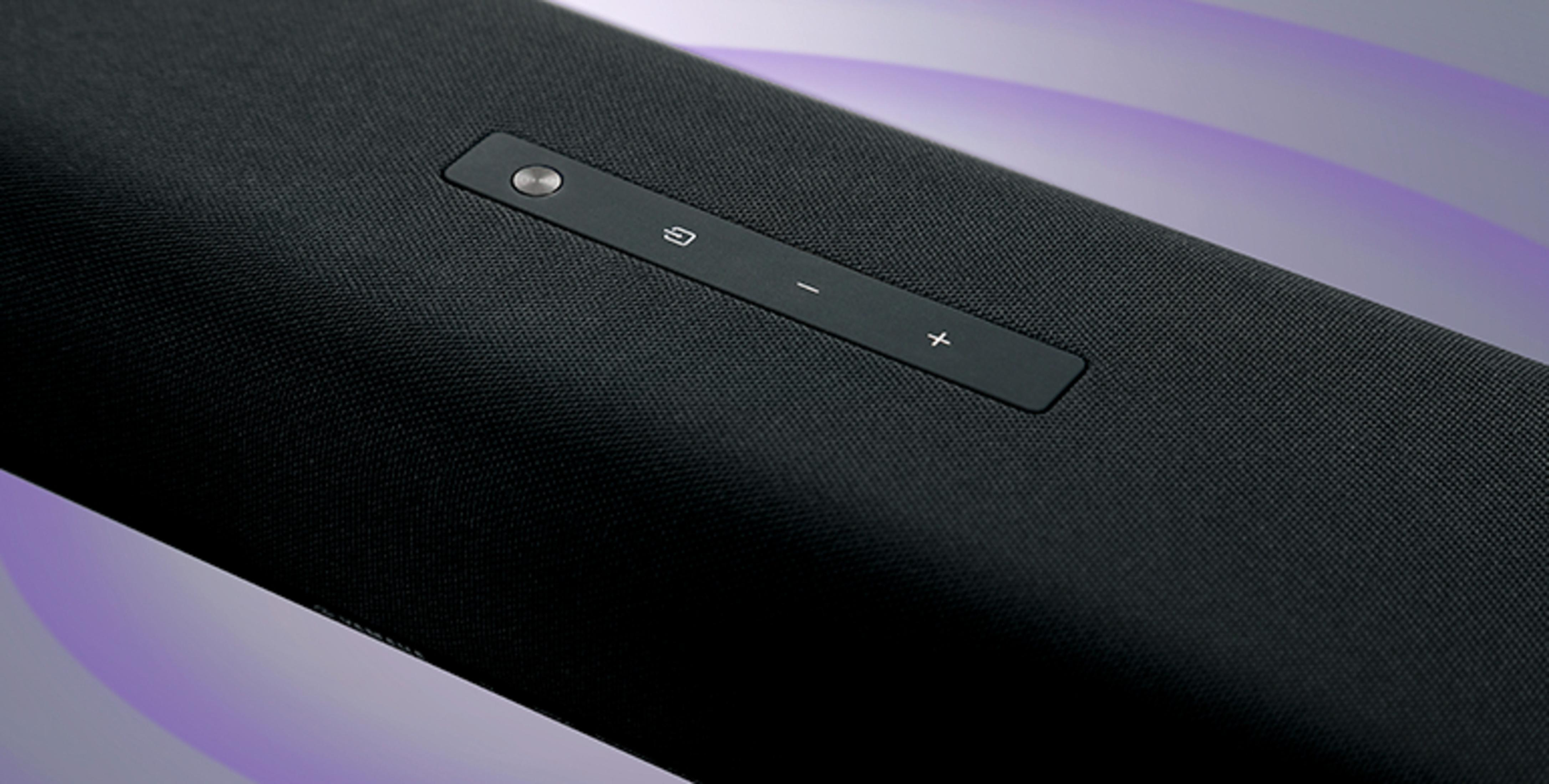 Close-up van een zwarte soundbar met knoppen, een grijs knoppenpaneel en een zwart mesh-oppervlak.
